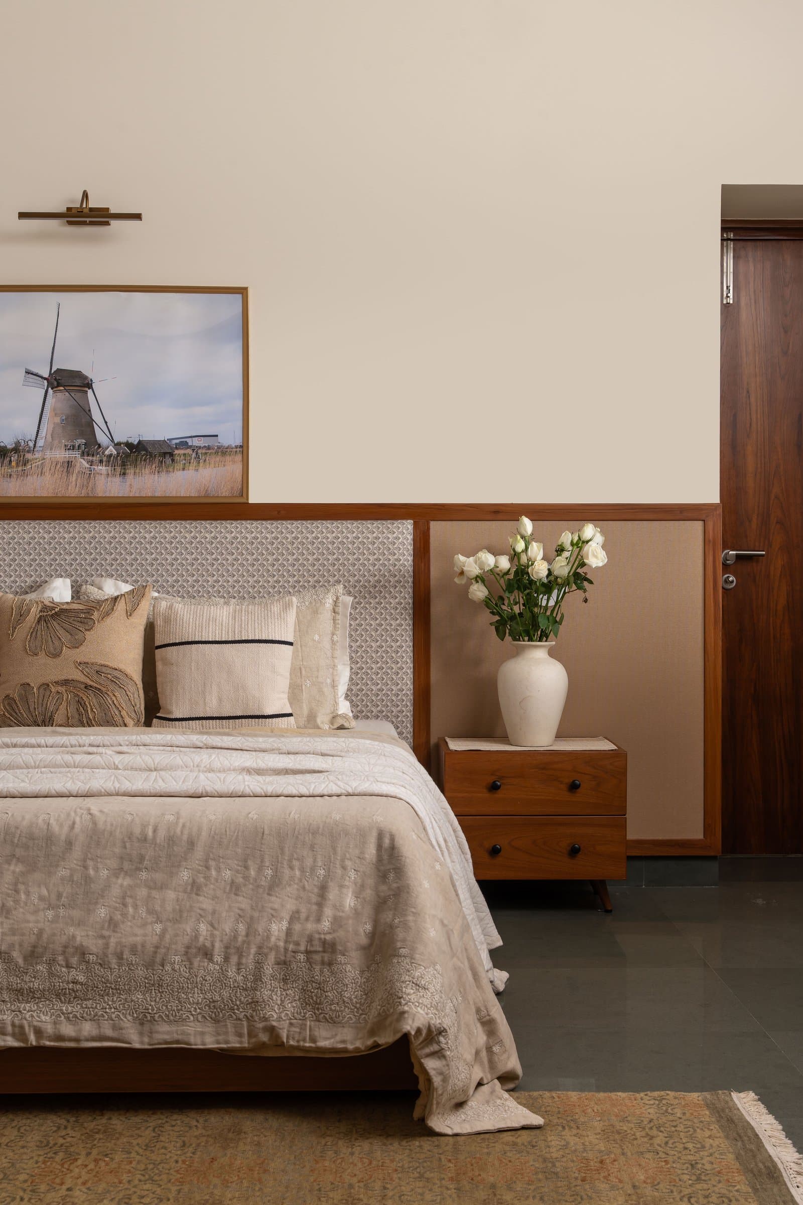 The master bedroom, where a timber wainscot panel and a brass-lit landscape photograph compose a wall of unusual, unhurried intention