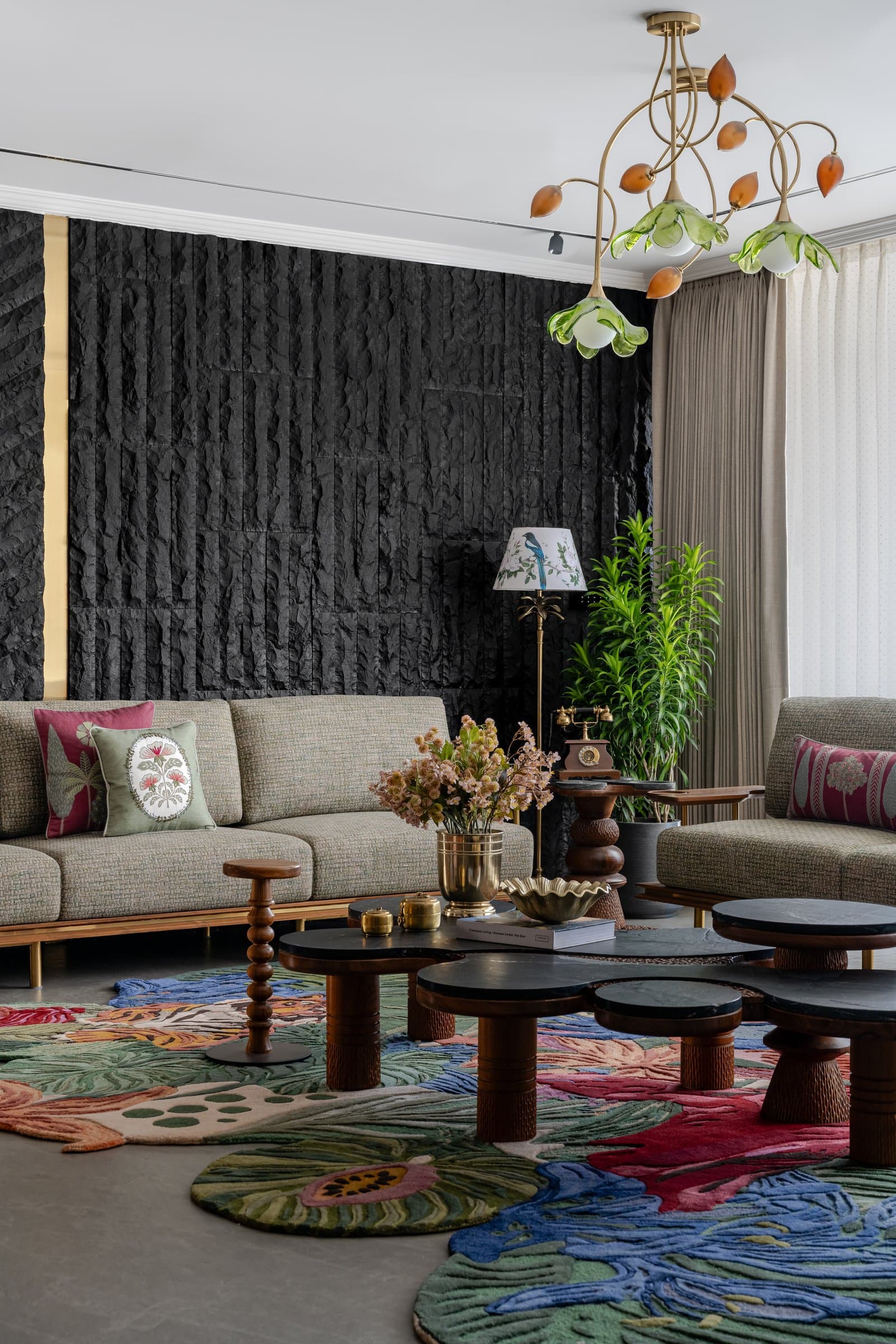 Wing A's living room: rough-hewn black stone, a botanical chandelier, and clustered marble coffee tables on a hand-tufted rug