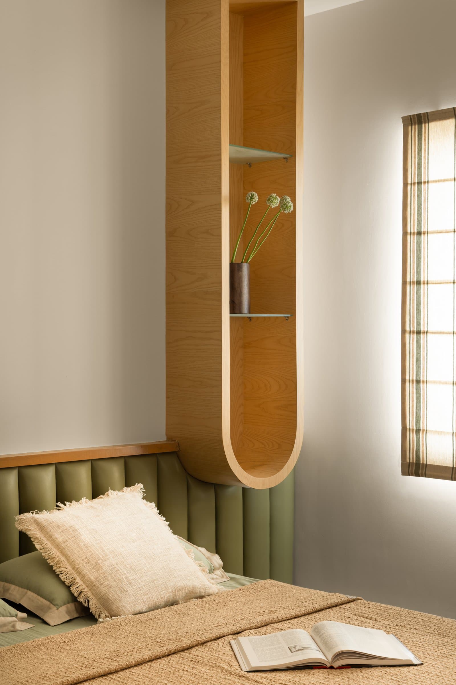 A bedside detail in the daughter's room: a rounded oak niche and olive-toned headboard share the same material conviction as the rest of the villa