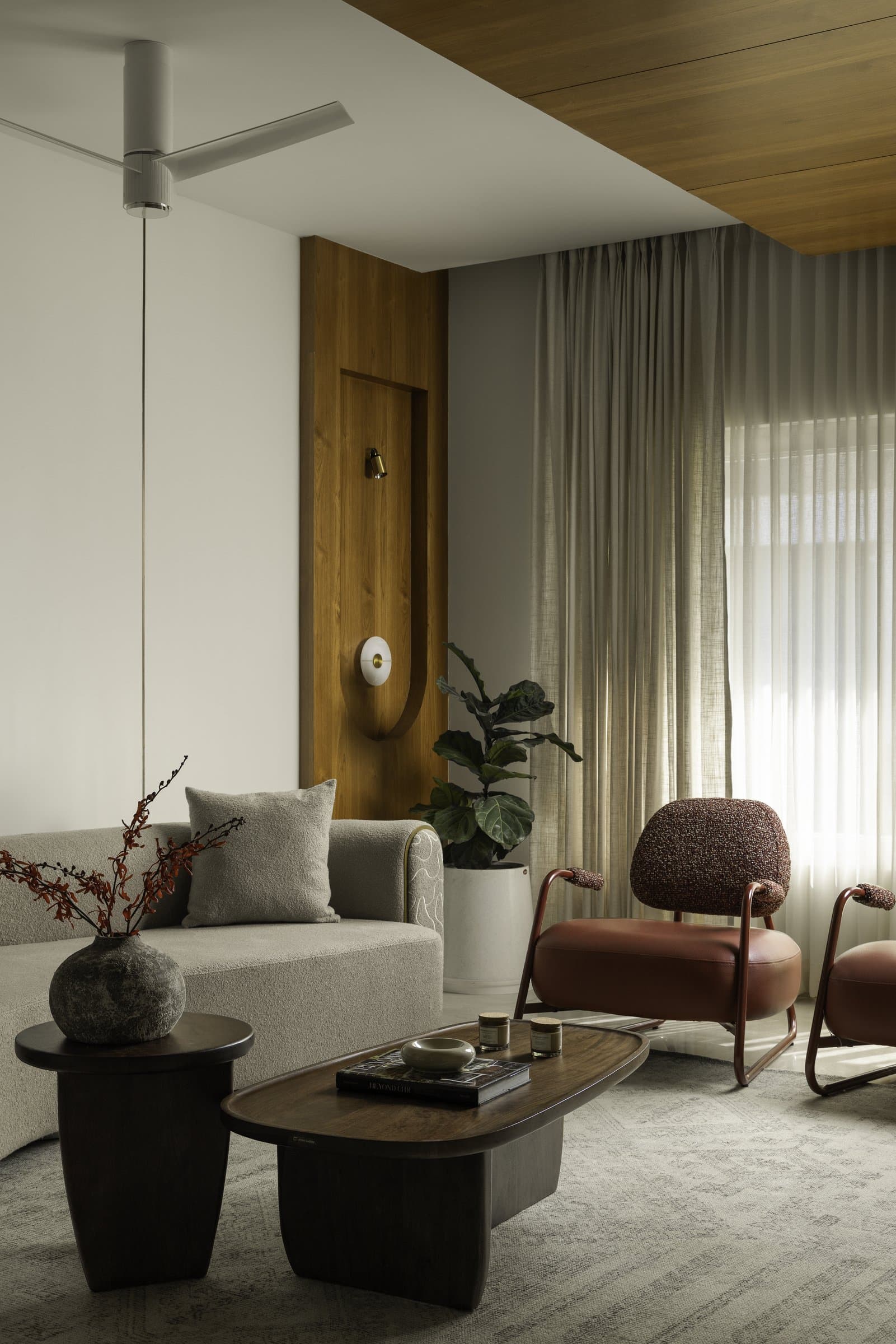 A closer view of the living room seating, with rust-toned accent chairs and a timber-clad wall panel acting as the room's quiet anchor