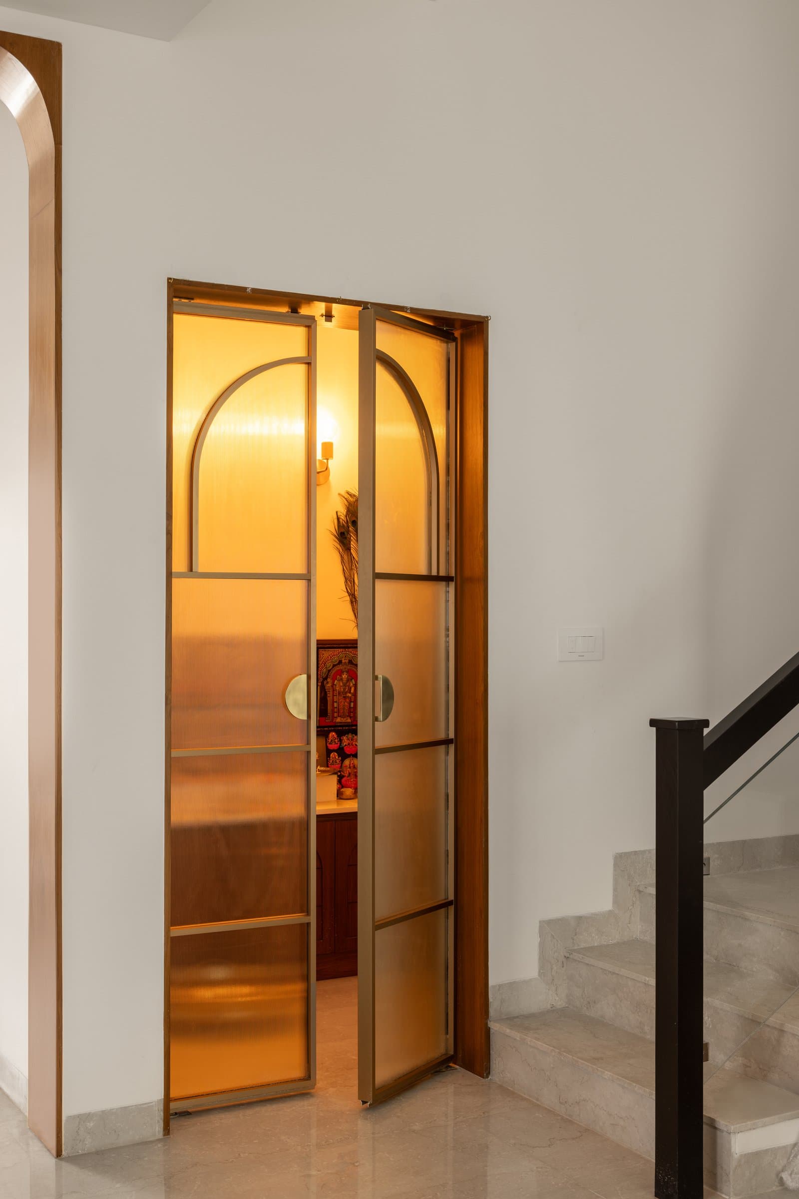 The pooja room, enclosed by arched amber glass-and-metal doors that filter light with quiet reverence