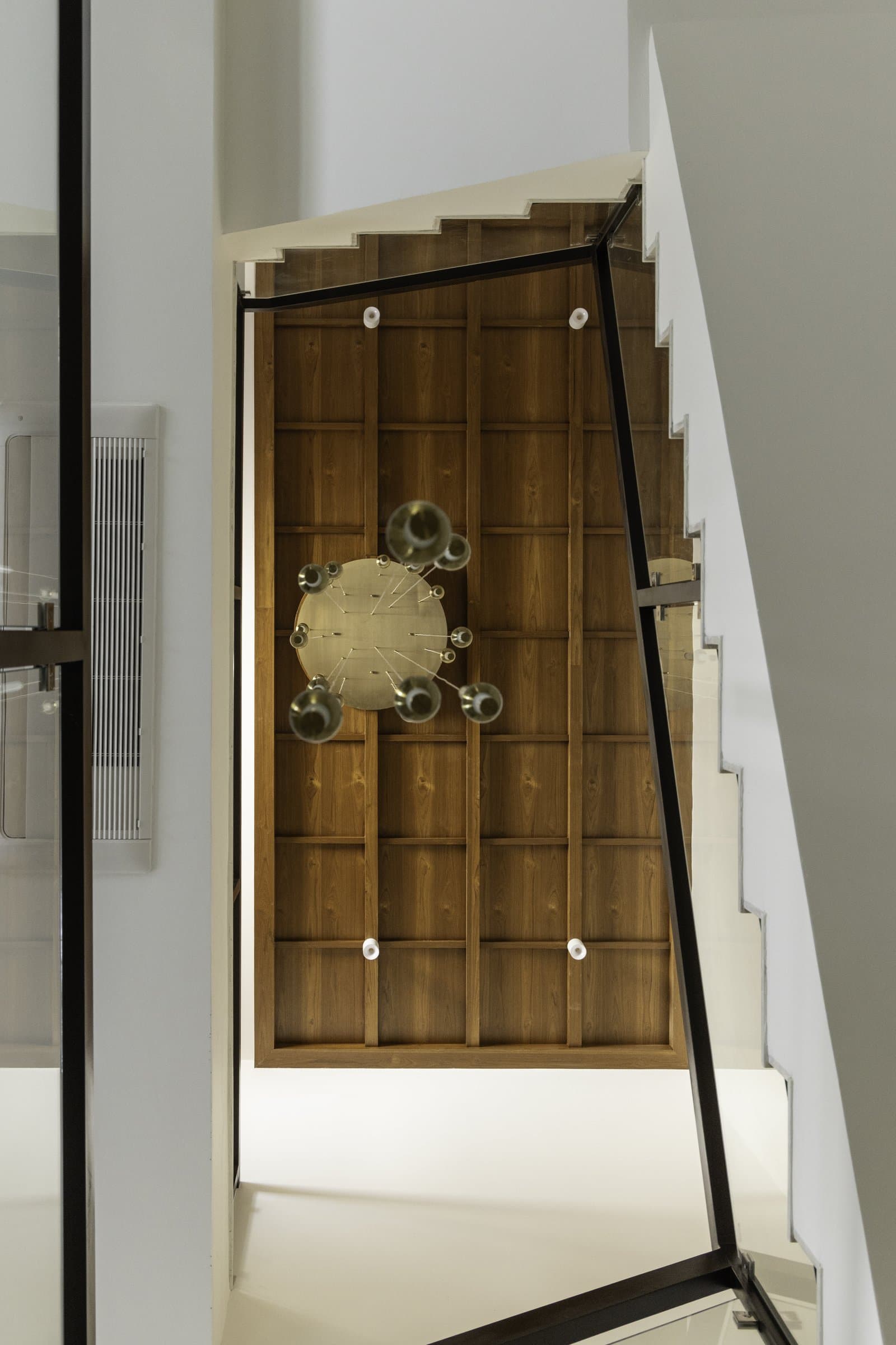 The staircase ceiling, transformed by a veneer grid and suspended brass chandelier into a spatial event