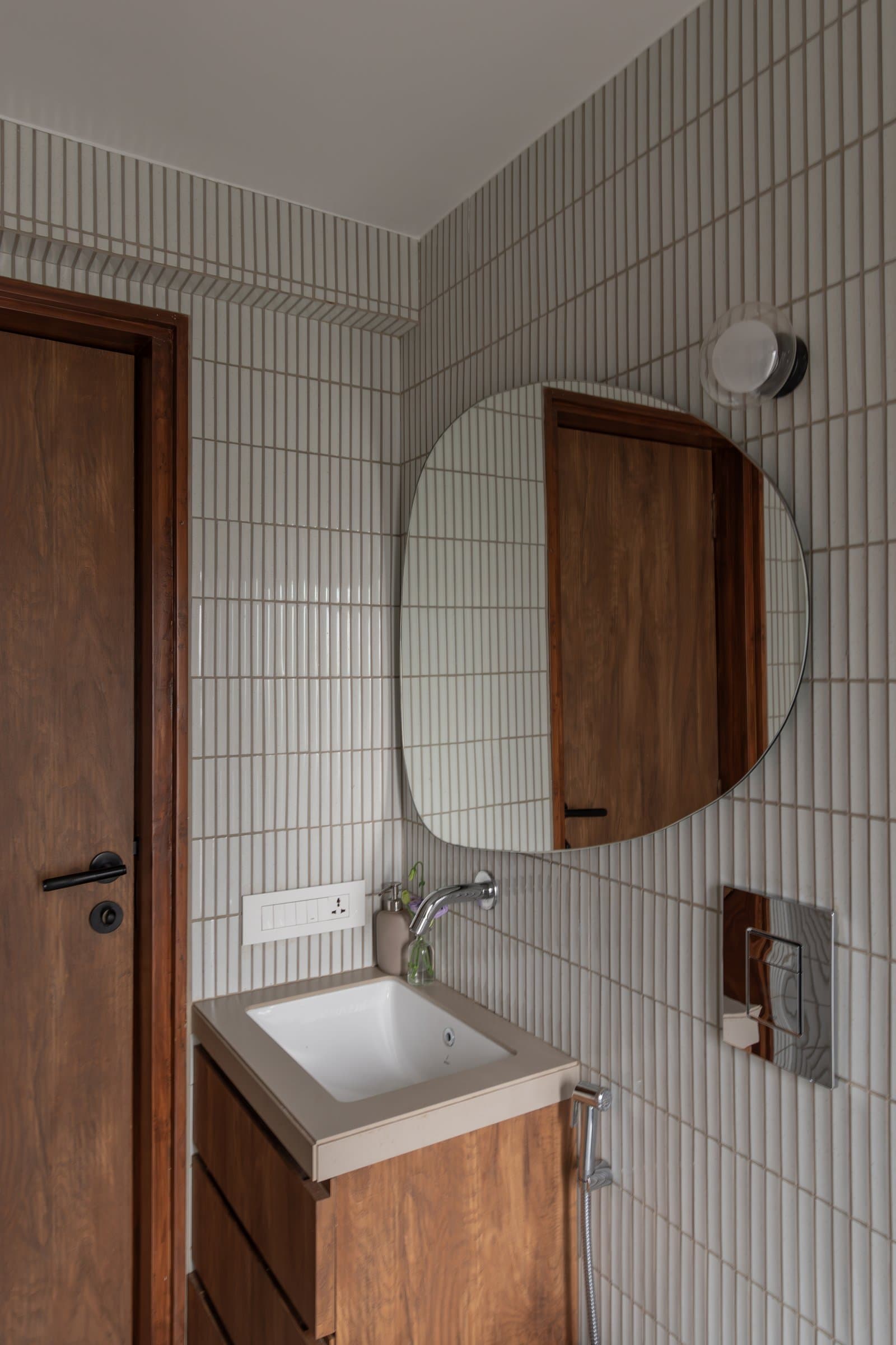 The bathroom, where stacked finger-tile elongates the room and a pebble-shaped mirror introduces its only curve