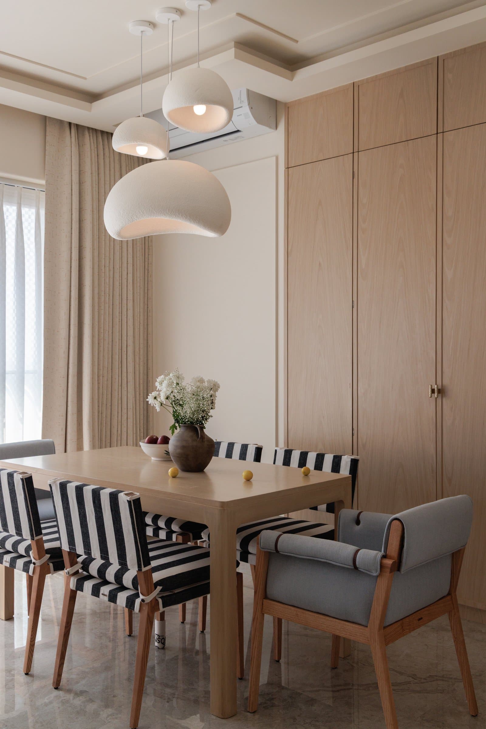 The dining zone, with textured white pendants and striped upholstery introducing a graphic counterpoint to the timber palette