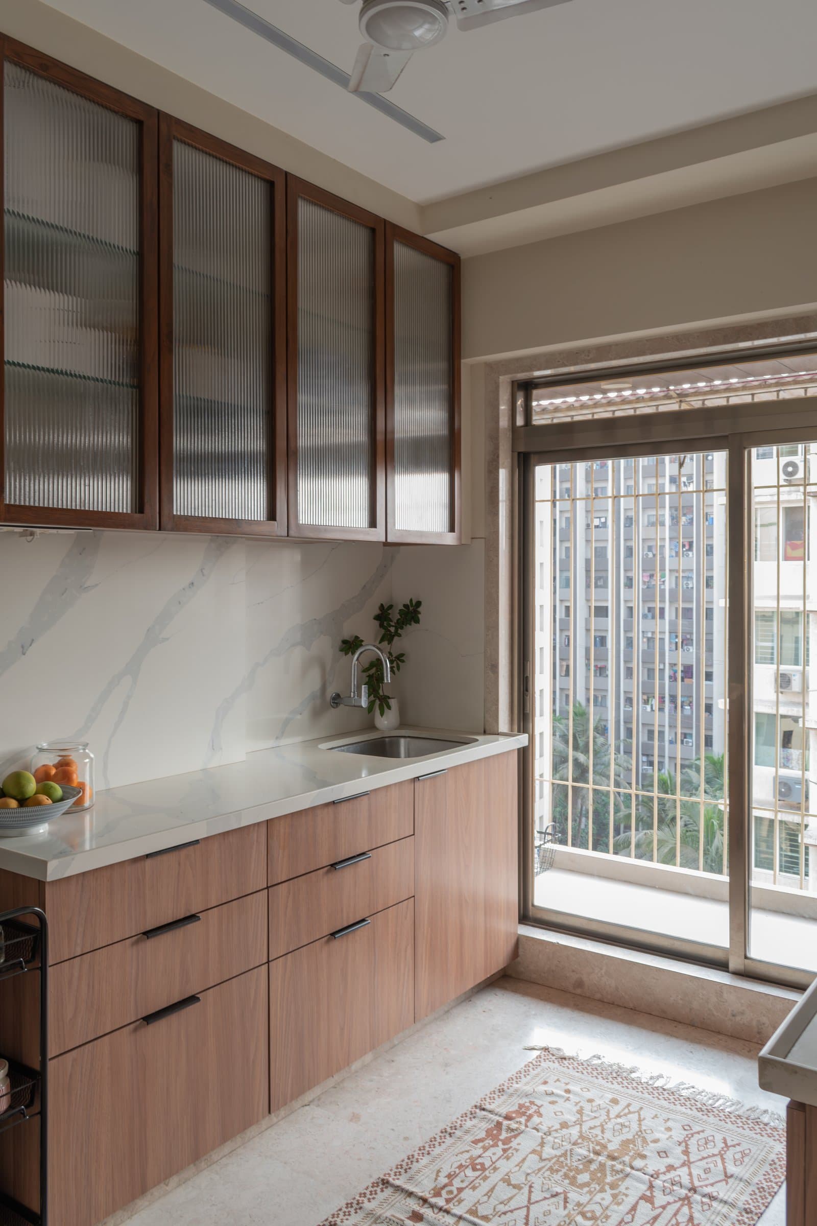 The kitchen, scaled to a couple: warm wood cabinetry, a marble-veined backsplash, and reeded-glass upper units
