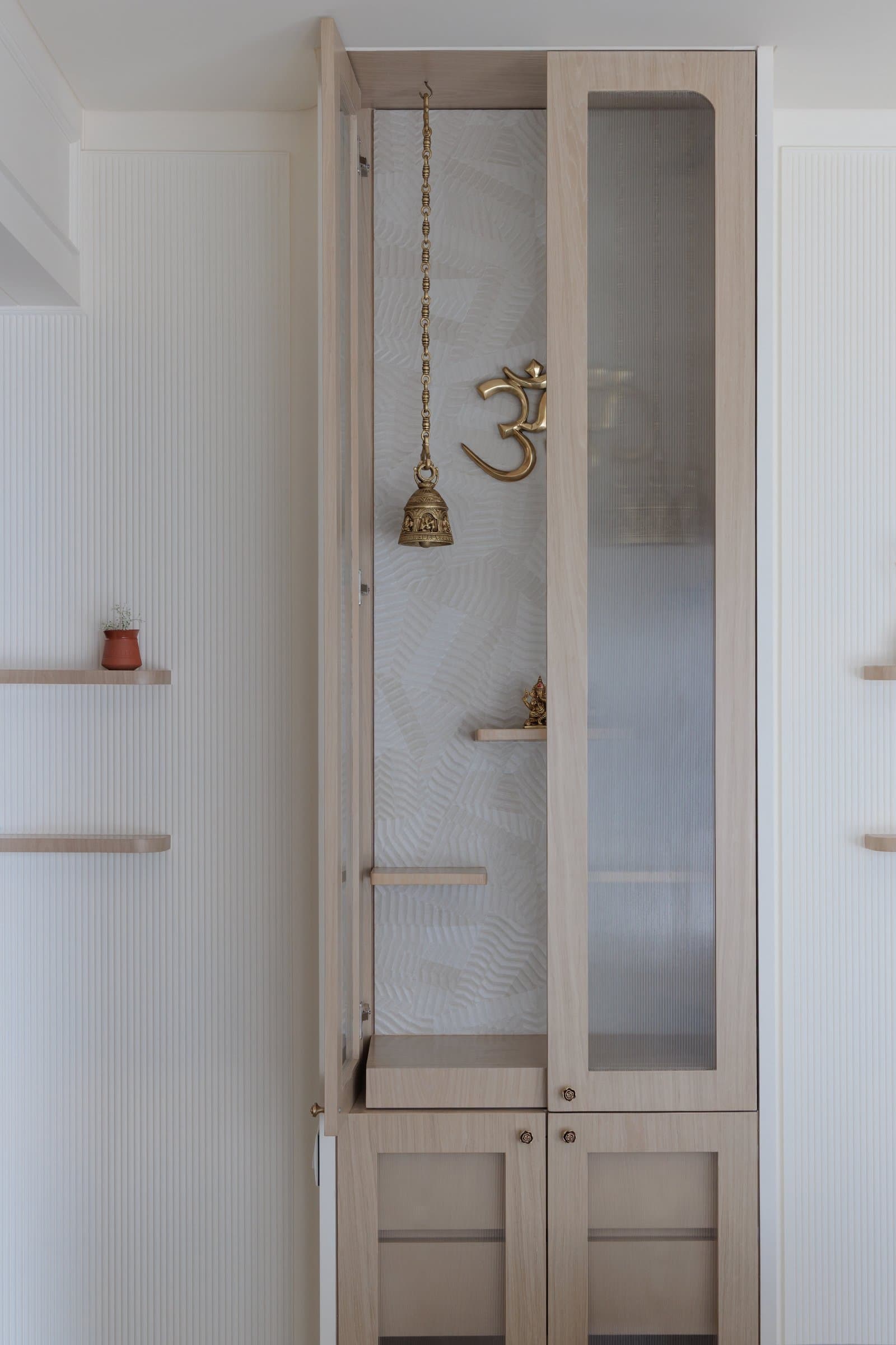 The mandir, with fluted glass shutters and brass accents, occupying its wall with architectural conviction