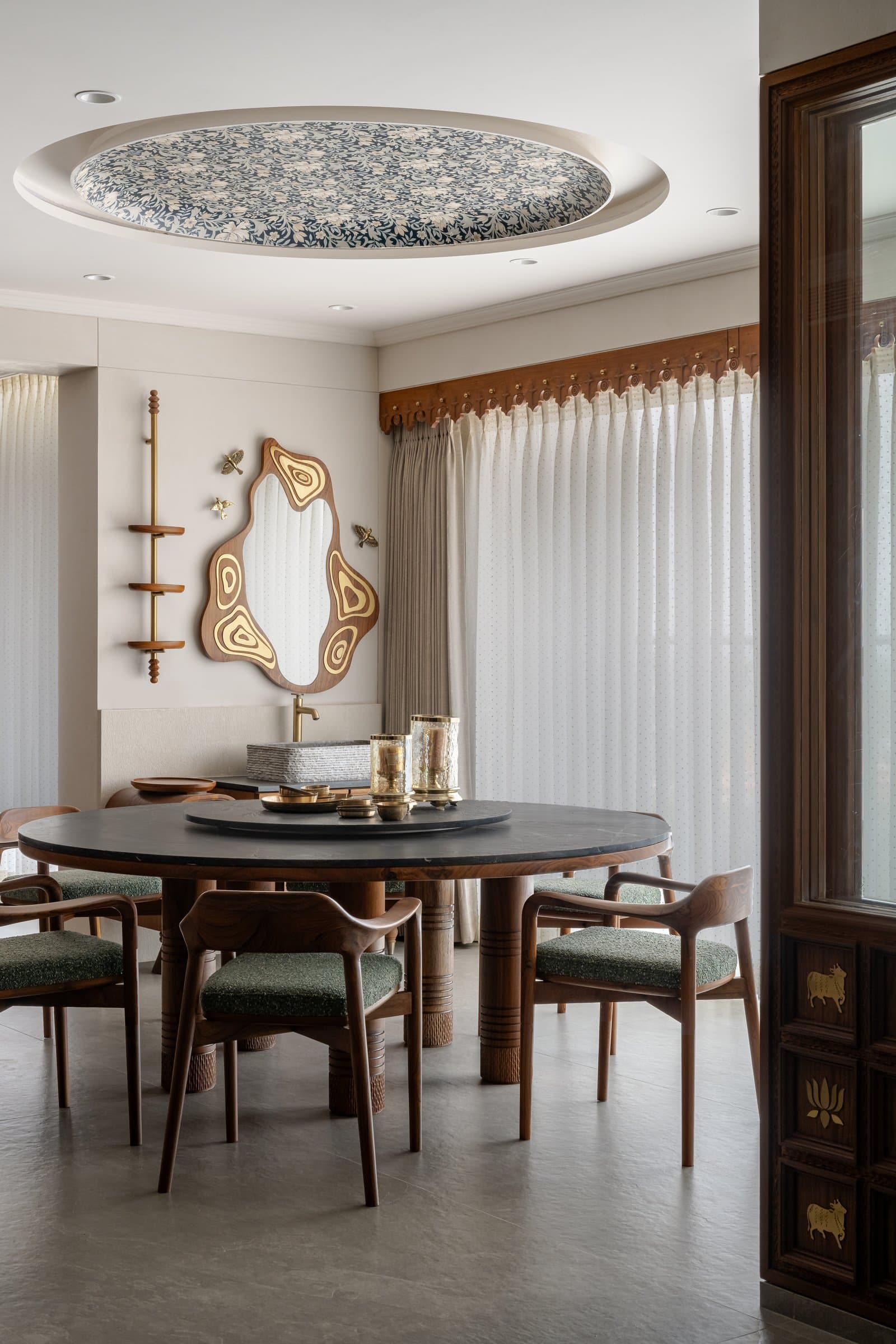 Wing A's dining area beneath a recessed floral ceiling medallion, the glass-walled pooja room visible beyond