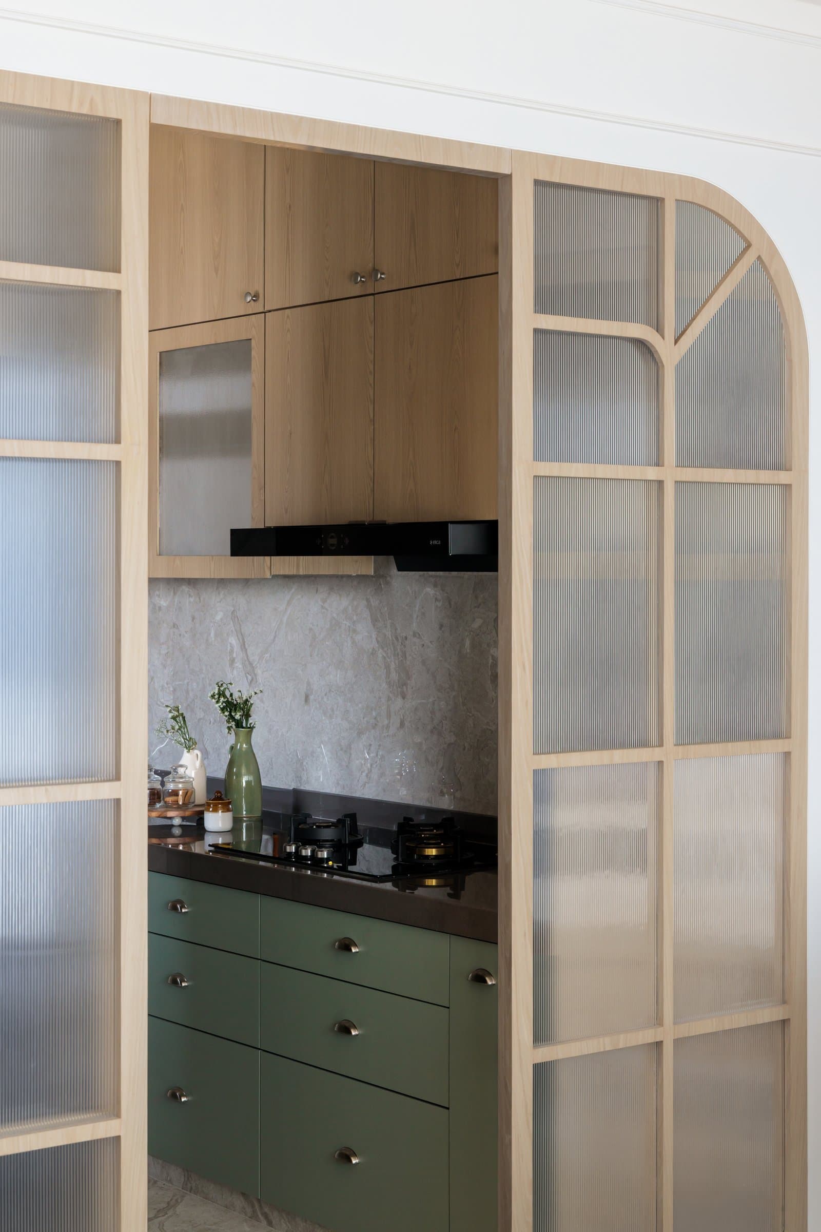 The kitchen through the arched frame: soft green base cabinets and a stone backsplash shift the palette for the first time