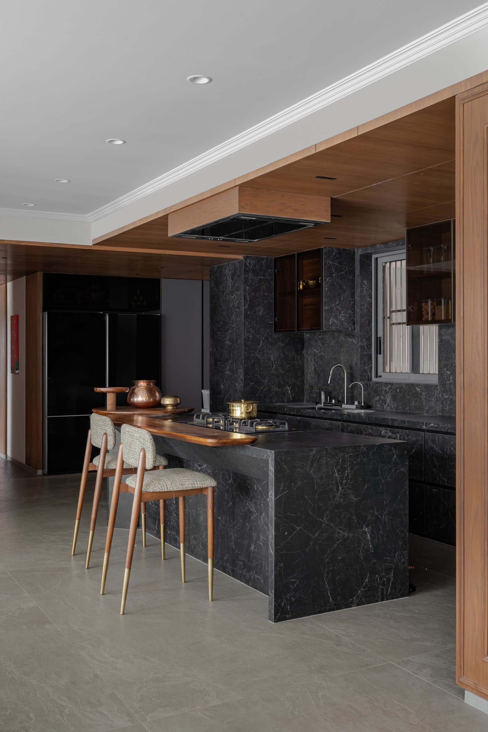 The kitchen in veined dark stone, its live-edge timber breakfast bar extending the warmth of the common areas into the workspace