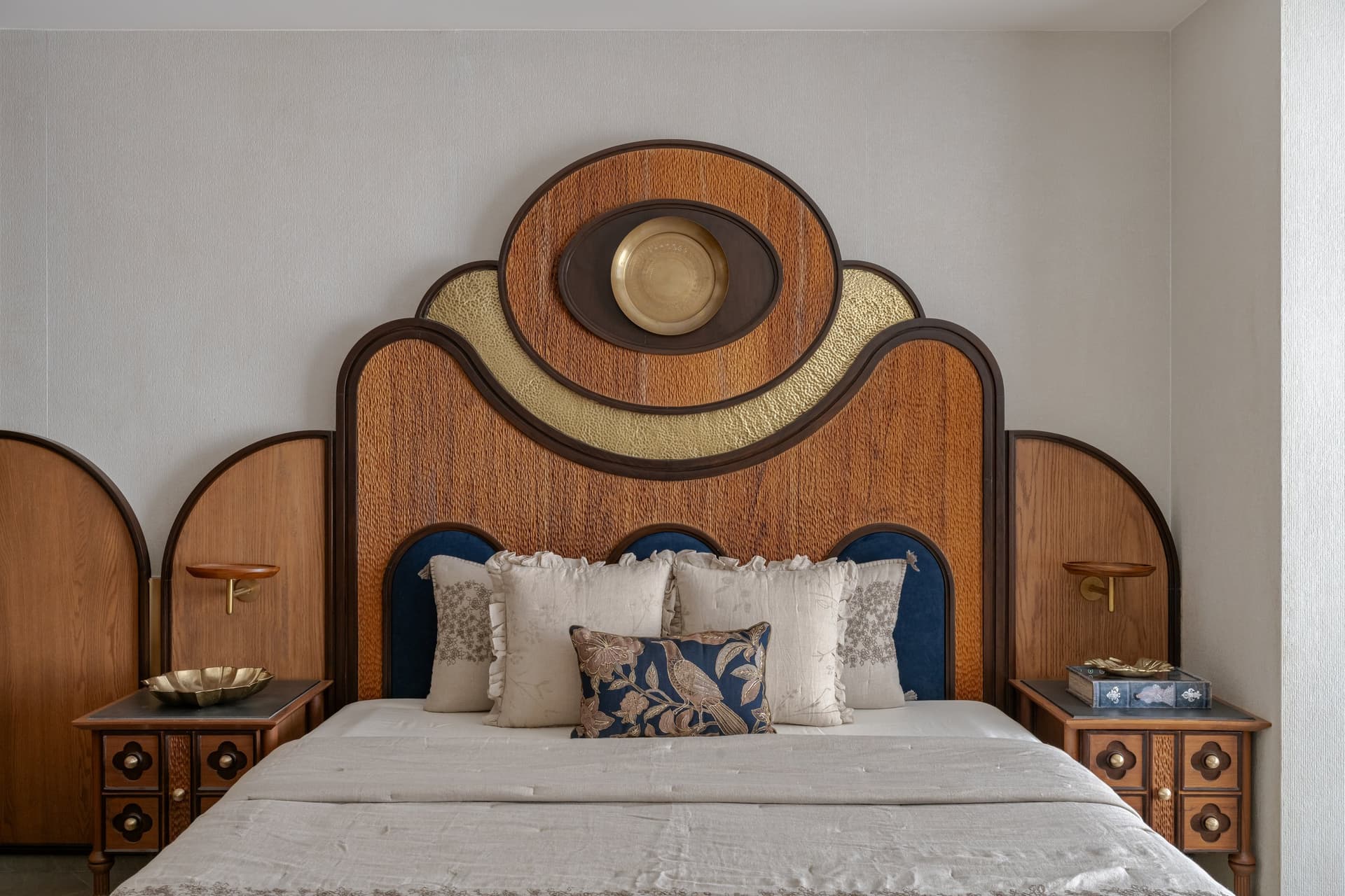 Wing A's master bedroom headboard: layered arches of carved timber and hammered gold, crowned by a brass medallion