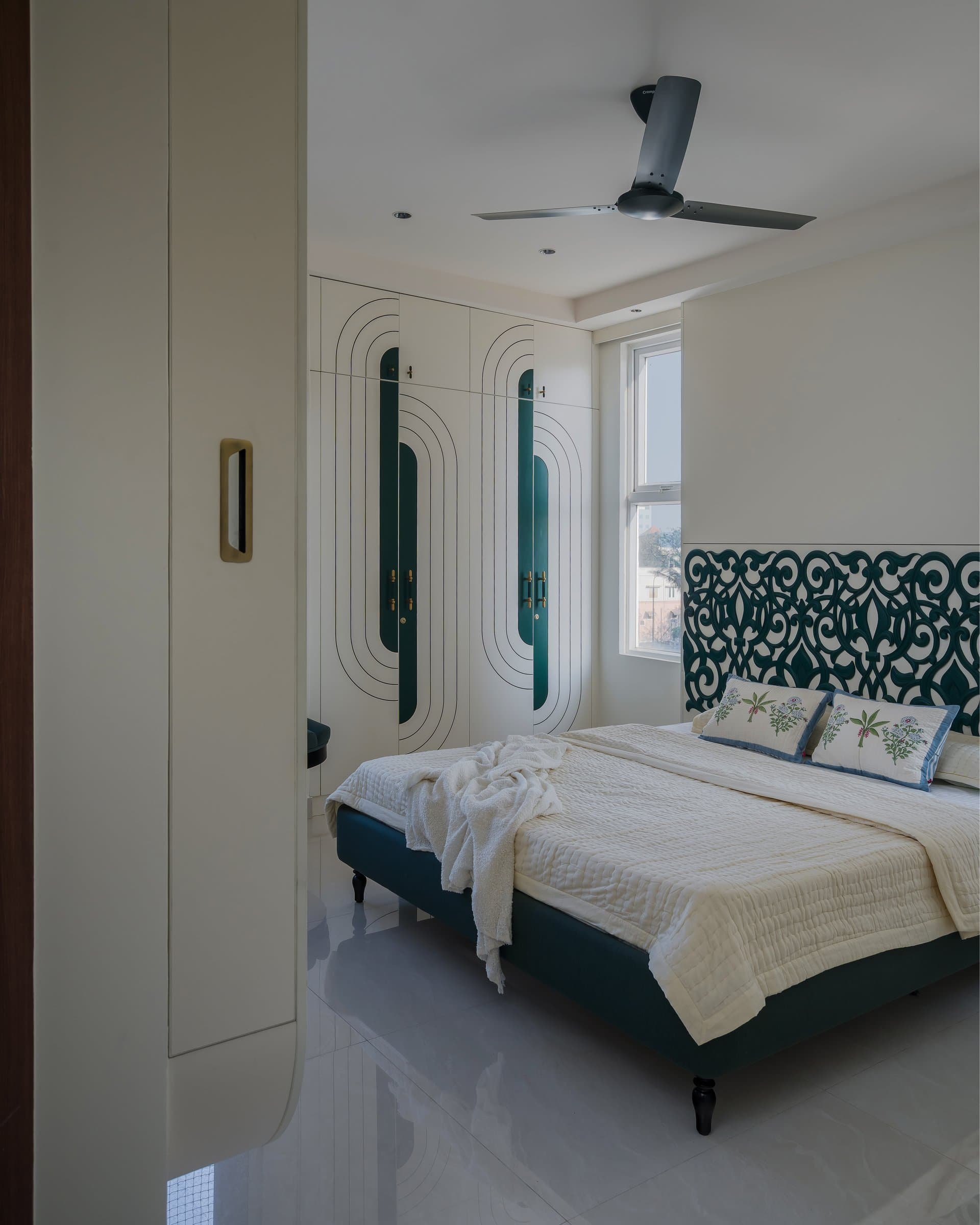 A second bedroom in teal and white, with a laser-cut scrollwork headboard and arc-detailed wardrobes