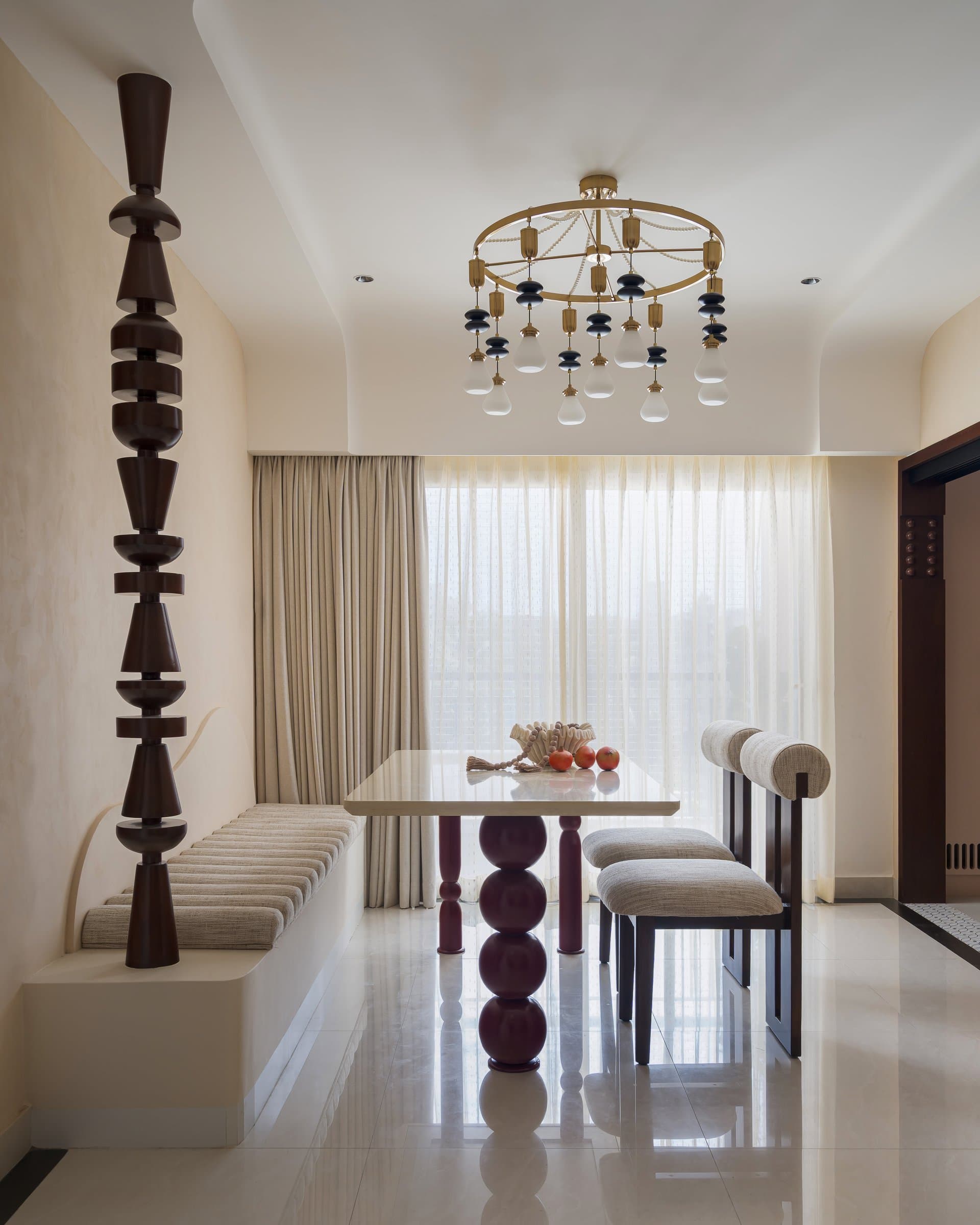 The dining area in full: stacked-sphere table legs, a brass and glass chandelier, and a built-in banquette create a space designed for lingering