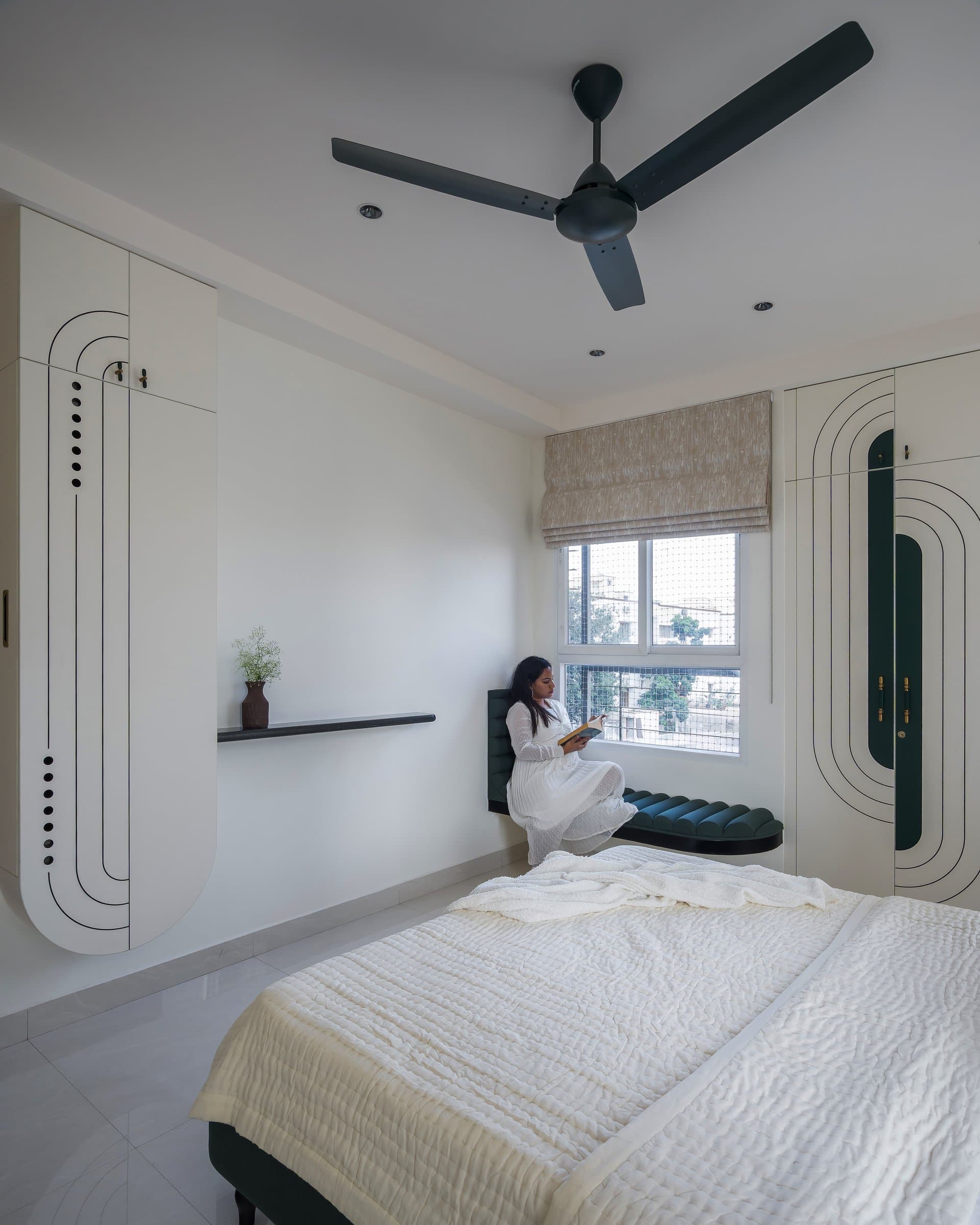 The second bedroom seen from the foot of the bed, with a built-in window seat and flanking storage walls framing a reading nook