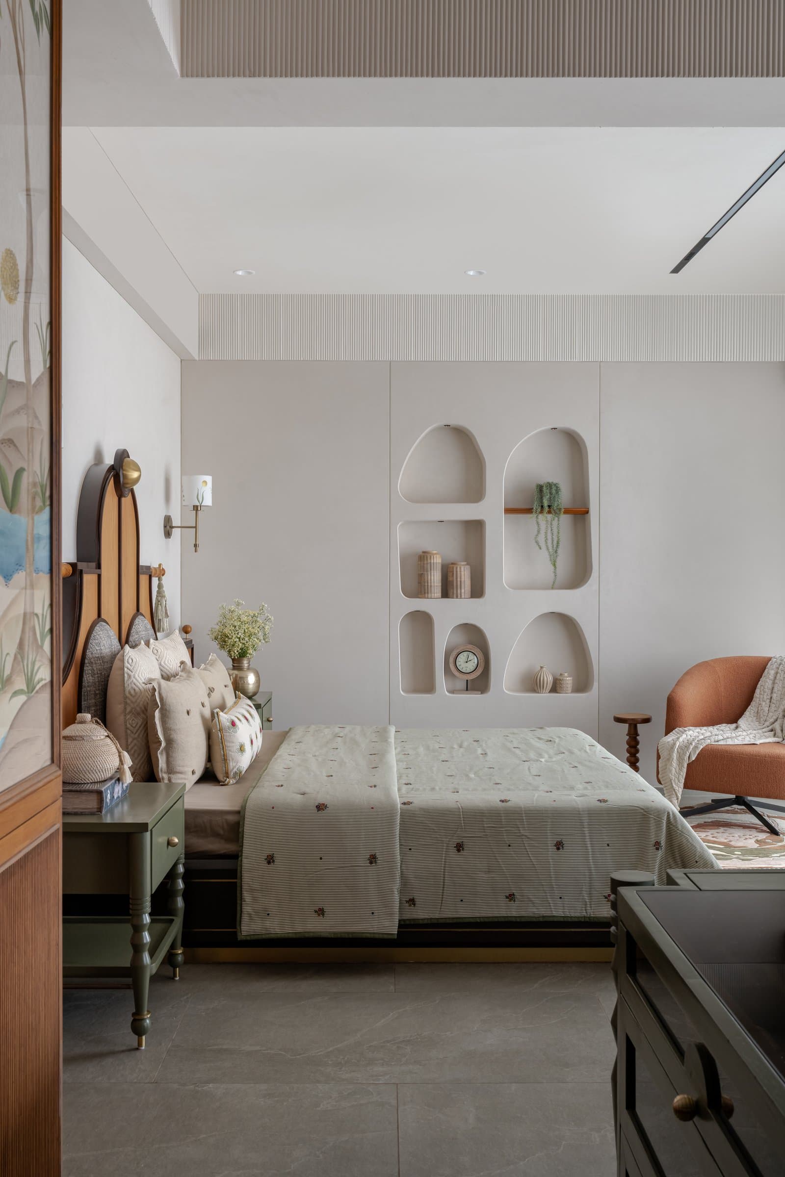 Dhruvi's bedroom: arched wall niches, a sage-green vanity island, and an accent chair in burnt orange against a muted cream palette