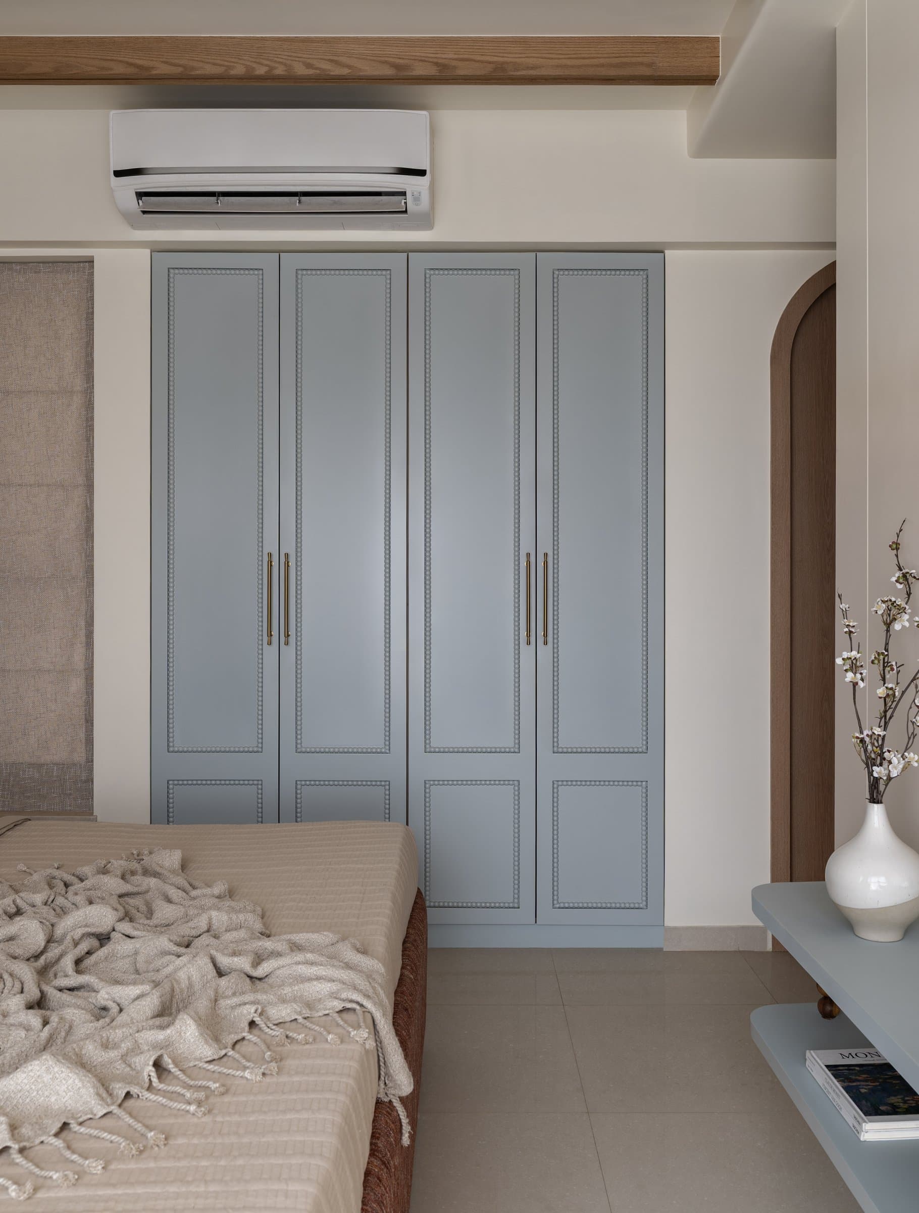 The powder-blue wardrobe, detailed with applied beaded mouldings and slim brass pulls, is the room's quiet workhorse