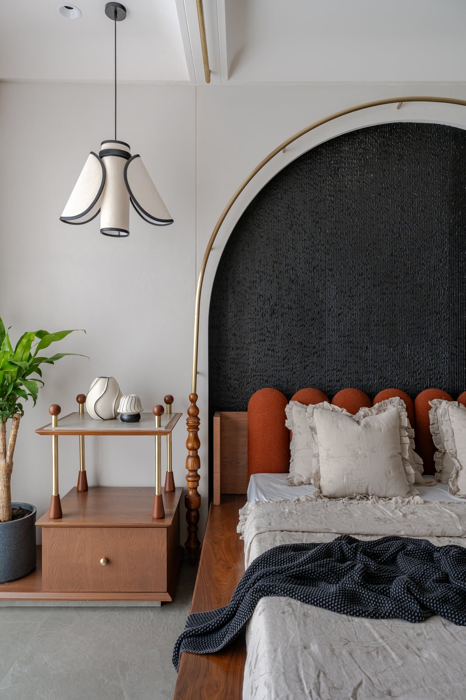 A younger bedroom's arched headboard in dark woven texture and brass, with terracotta-hued upholstered cushions