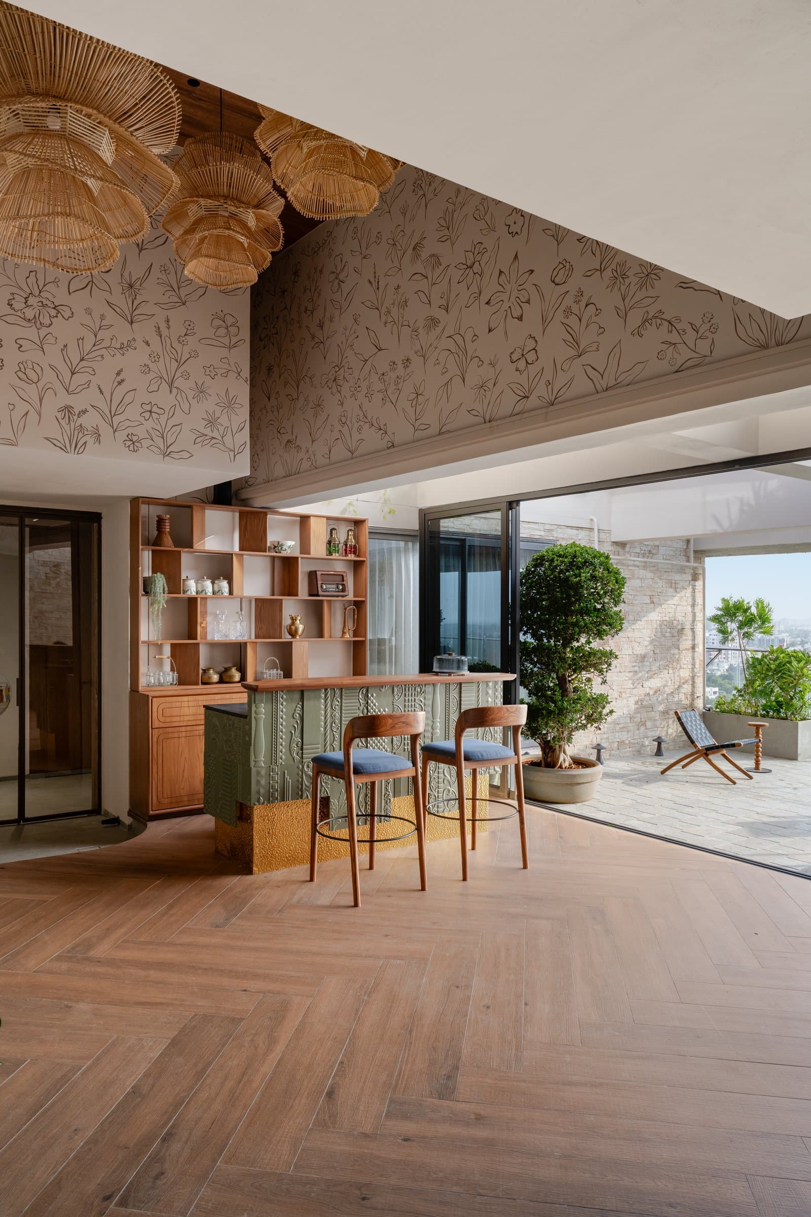 The deck's bar counter and herringbone timber floor opening through full-height doors to a stone-clad terrace above the city