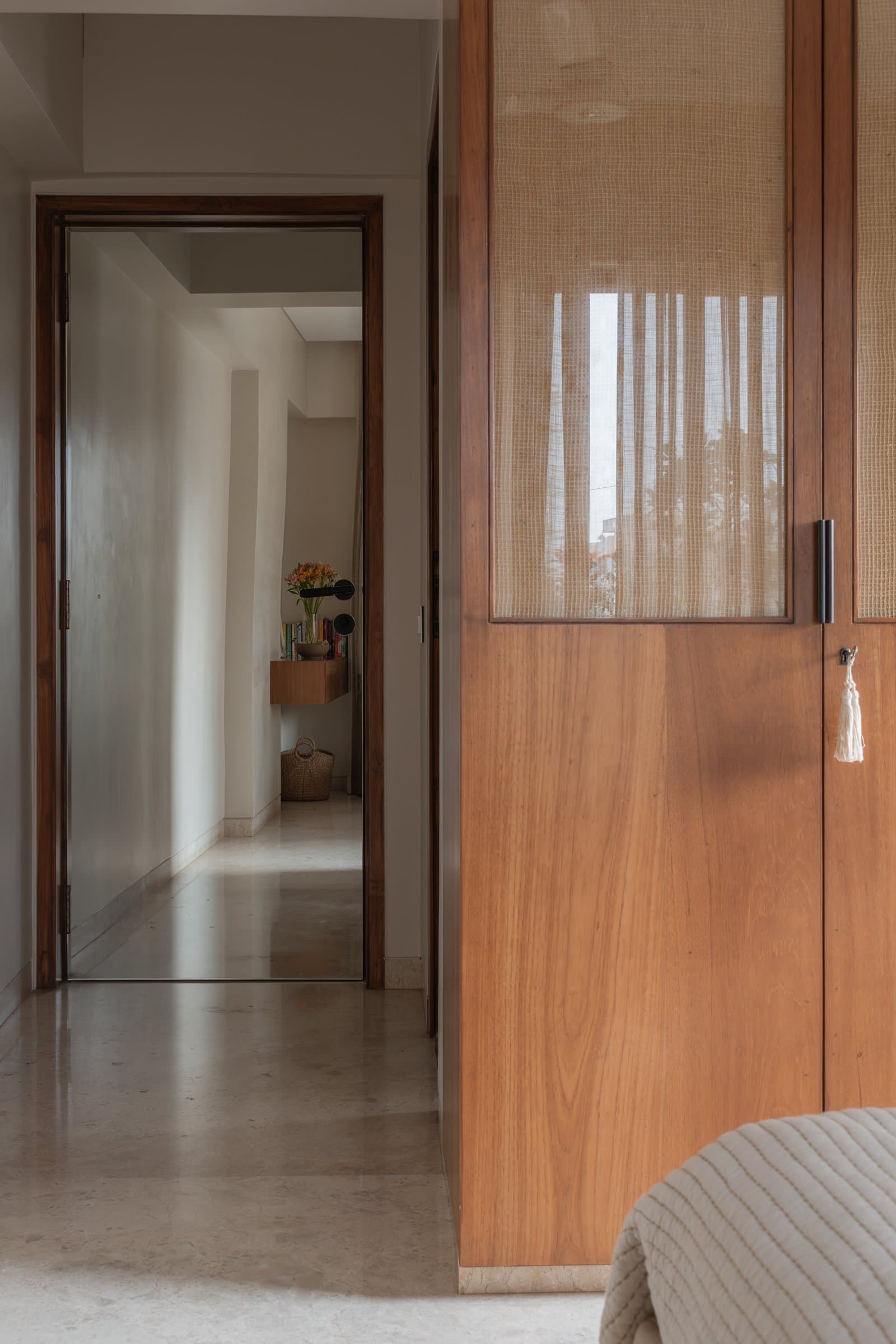 The passage between bedrooms, where a caned wardrobe admits a soft, screened light onto polished stone floors
