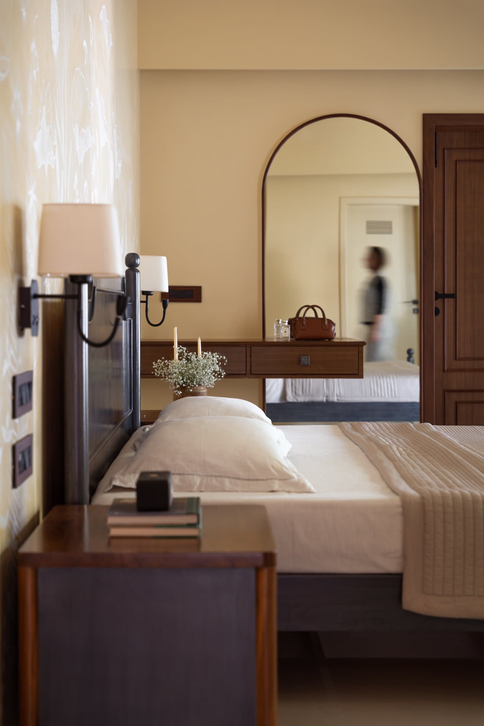 The same bedroom seen from the side, where a blurred figure at the door confirms the room's lived-in character