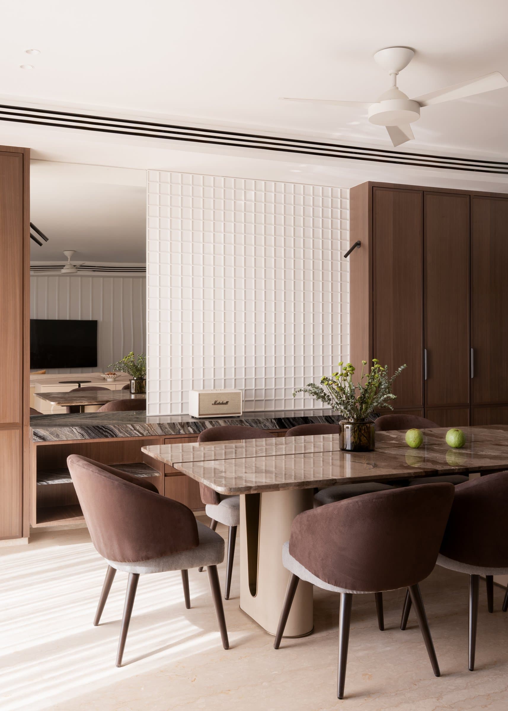 The square stone dining table on its sculpted pedestal, ringed by chairs in cocoa velvet and grey linen