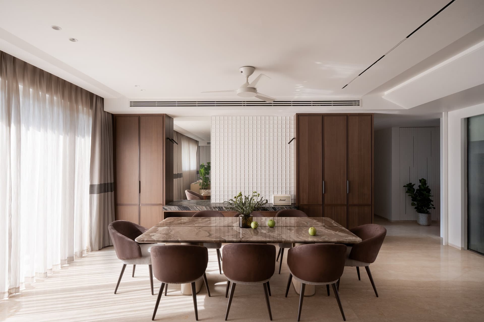 The dining room, anchored by a tall white tile-grid wall set between flanking walnut cabinets