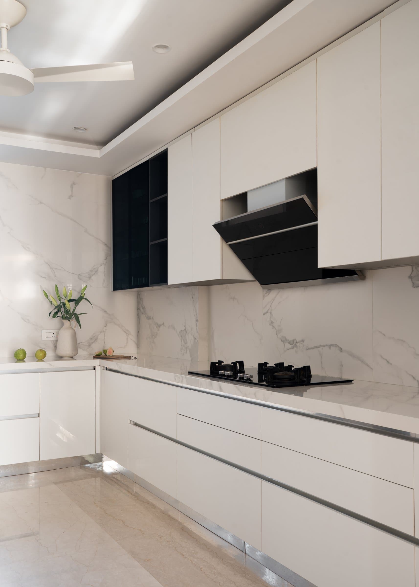 The kitchen, where book-matched marble meets matte ivory cabinetry, with a single graphite-glass cabinet as the only flourish