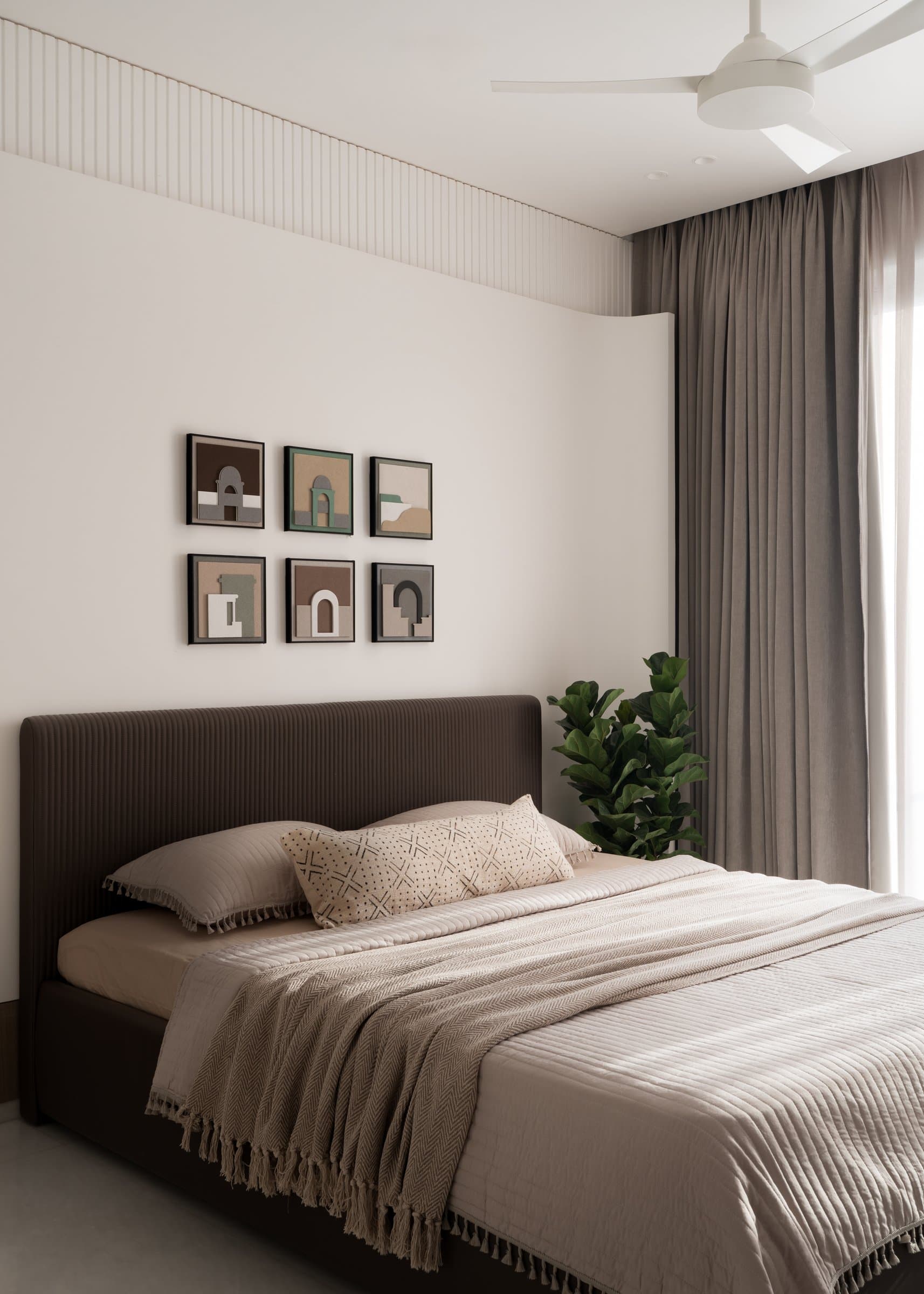 The grandparents' bedroom, dialled down to powder and putty, with a ribbed taupe headboard below a grid of small framed works