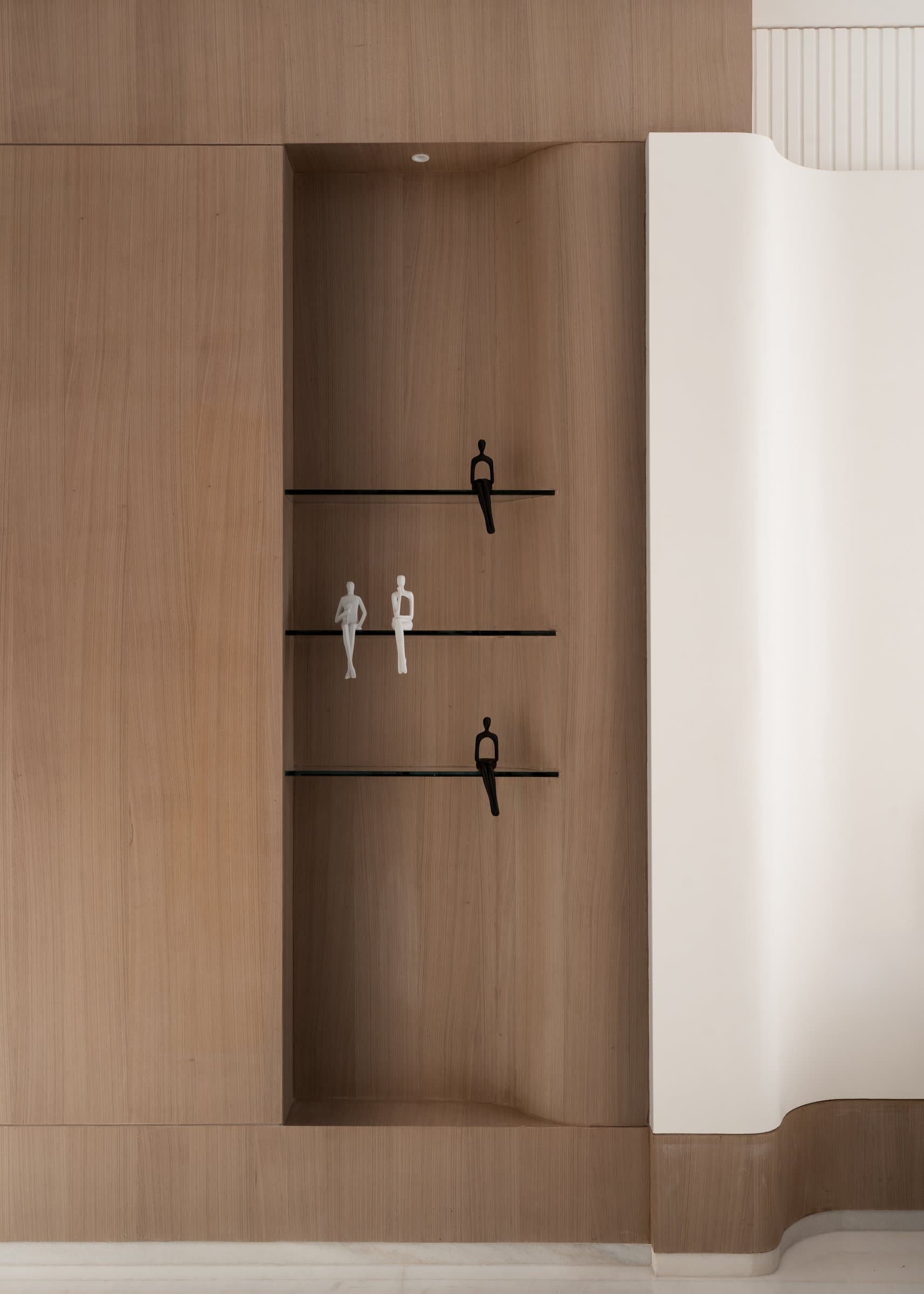 A carved oak niche holds two slim figurines on glass shelves, the kind of detail that rewards a second look