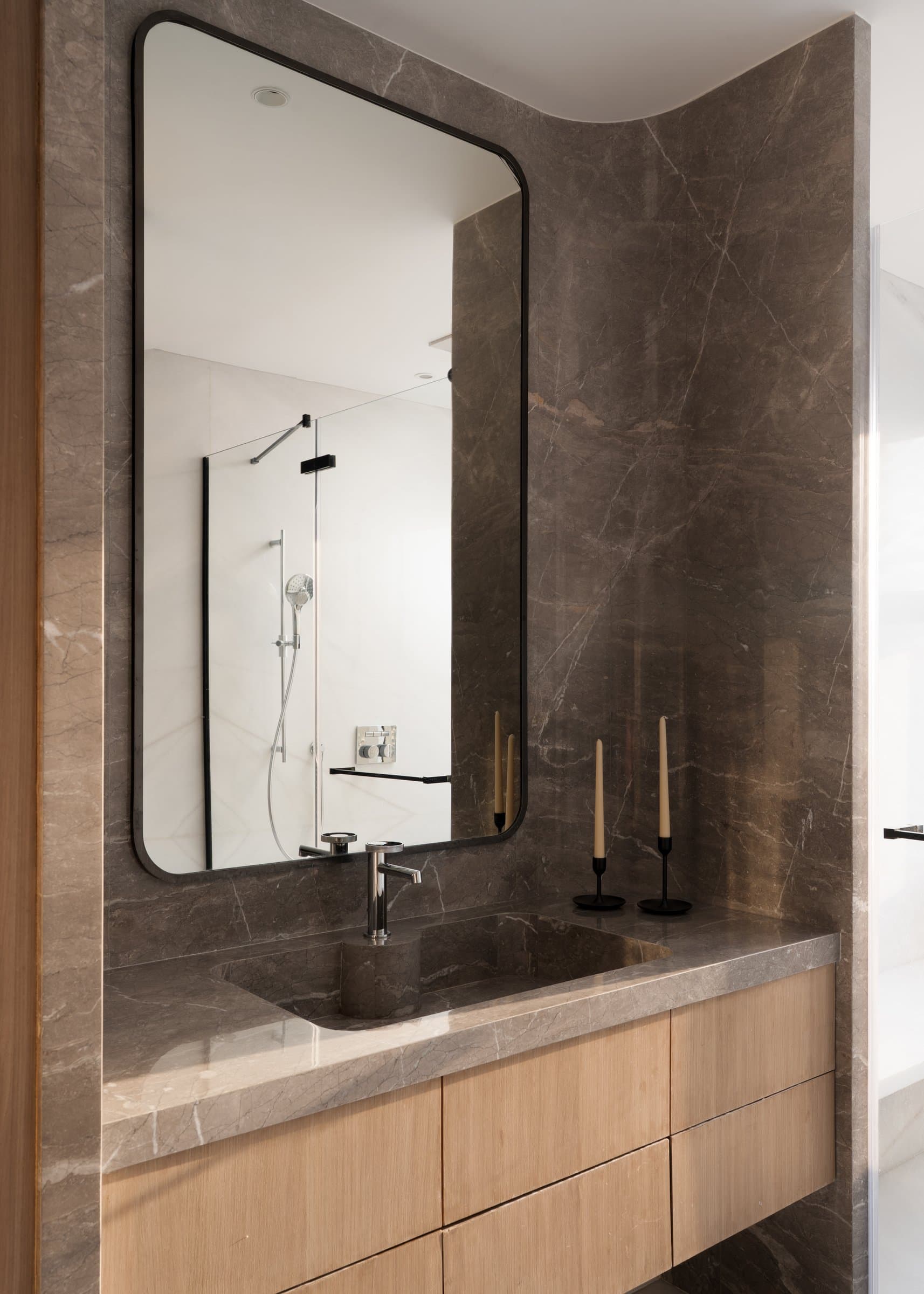 The master bathroom, where a single sweeping wall of veined grey stone curves into the ceiling above a light oak vanity