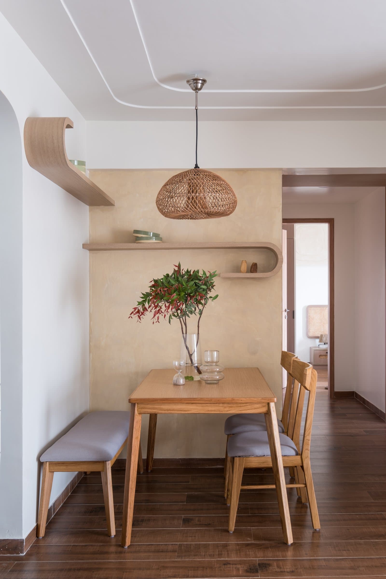 The dining nook tucked against a curved plaster wall, its looping timber shelving carrying the home's geometry
