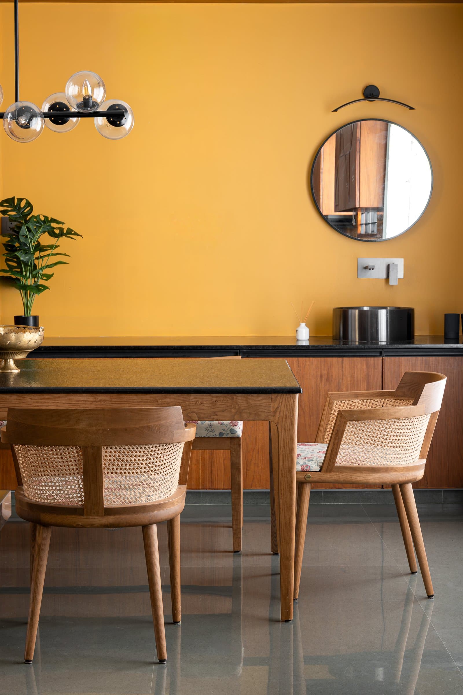 The dining zone seen from its opposite end, cane chairs and glass-globe chandelier in warm daylight