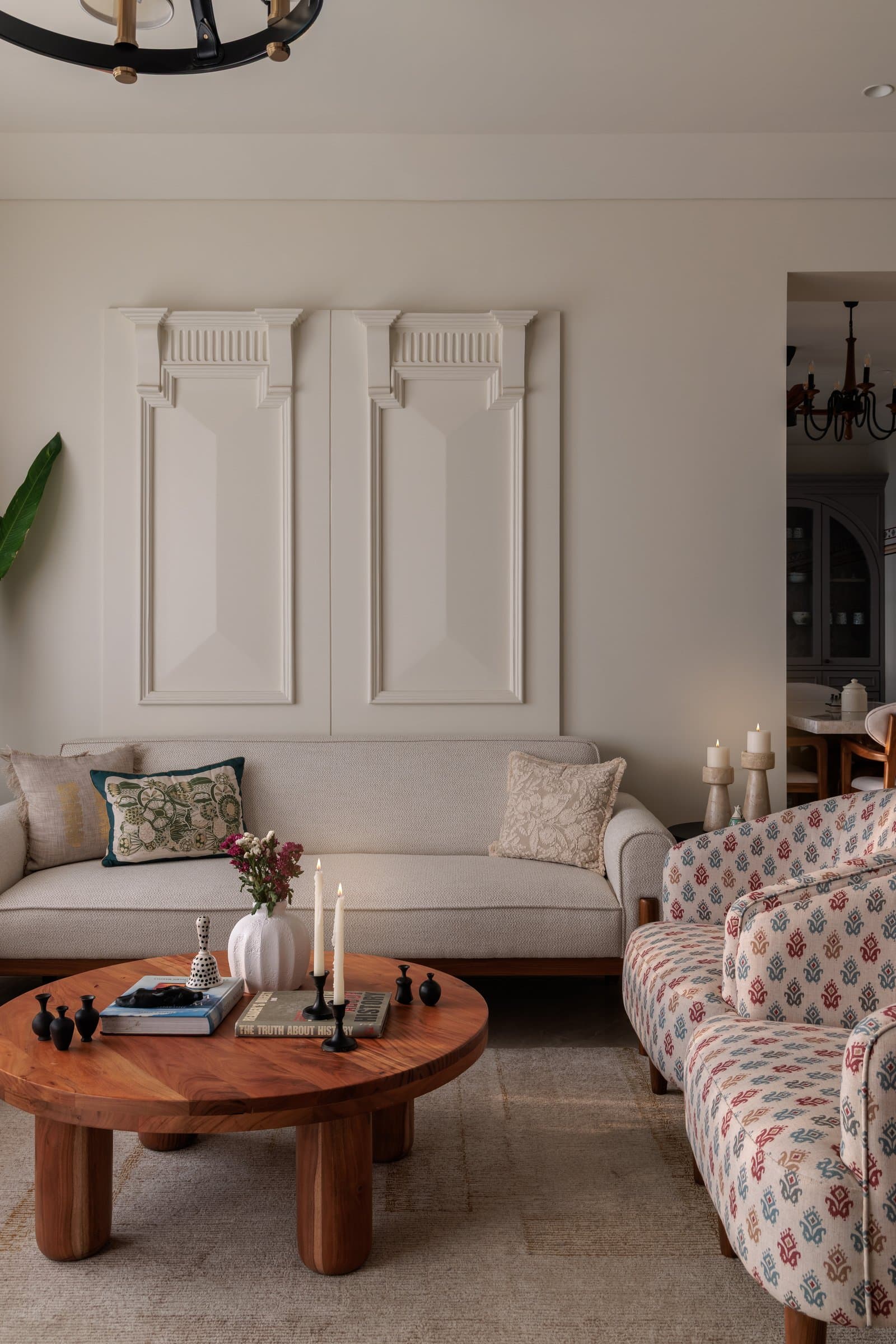 Classical wall mouldings in warm white anchor the sofa wall, letting the printed accent chairs carry the room's colour