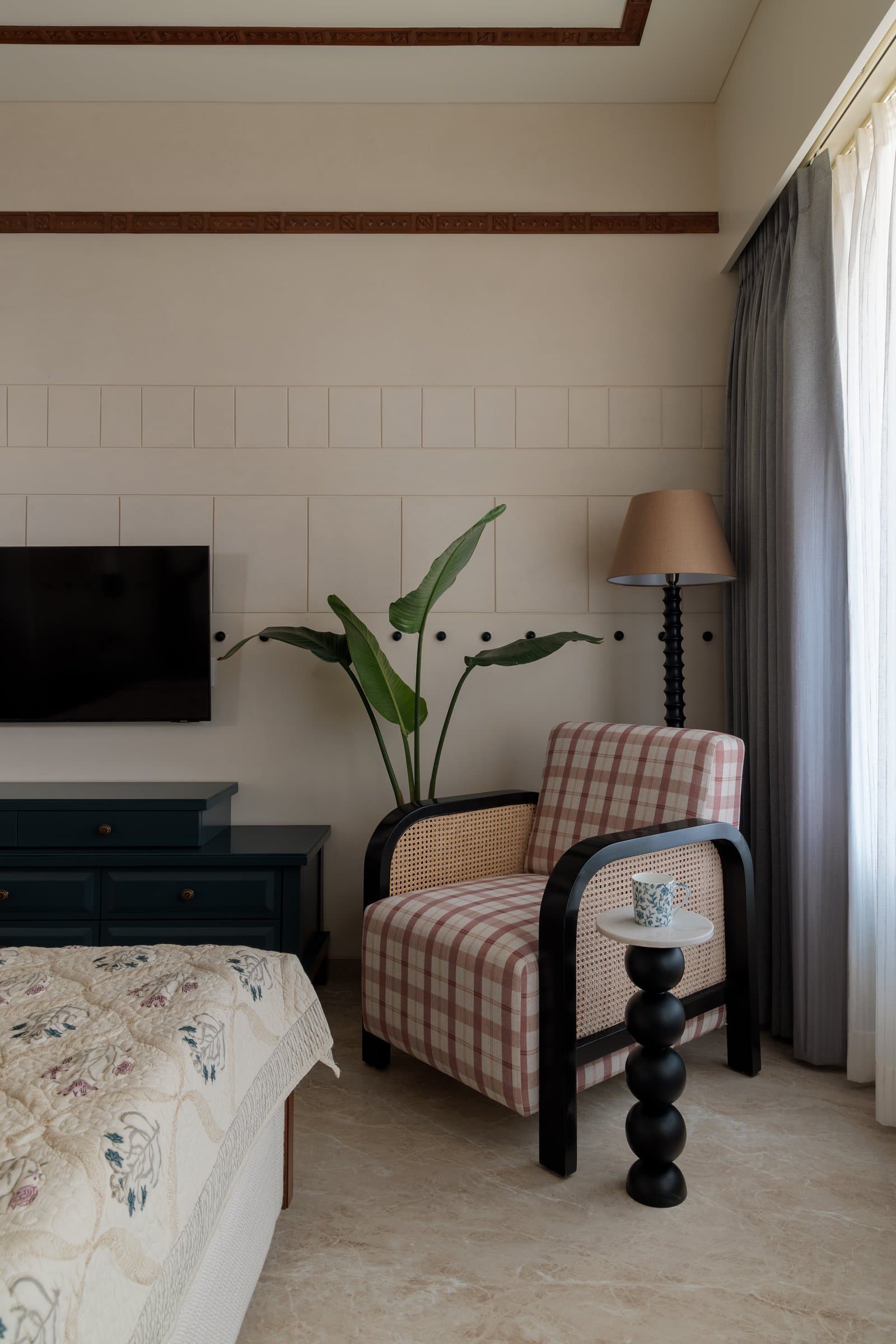 A gingham armchair with cane-woven panels and a sculptural side table anchor the master bedroom's reading corner