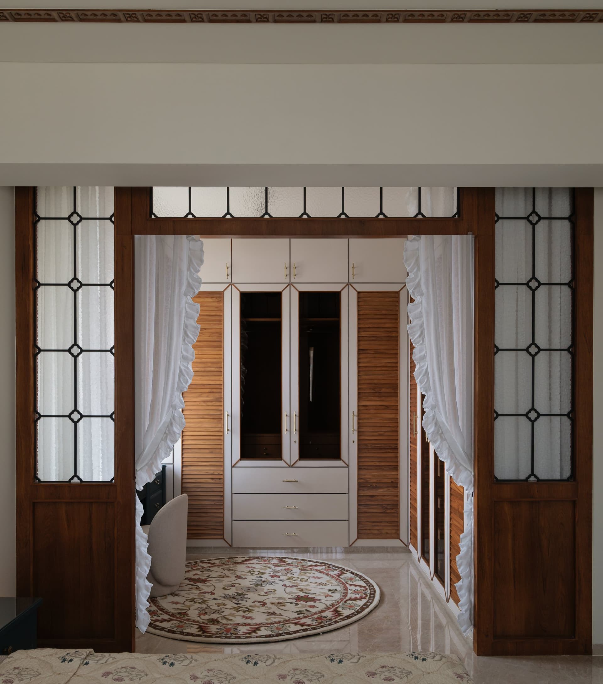 The dressing area, where louvred timber panels and mirrored wardrobe doors continue the bedroom's material language