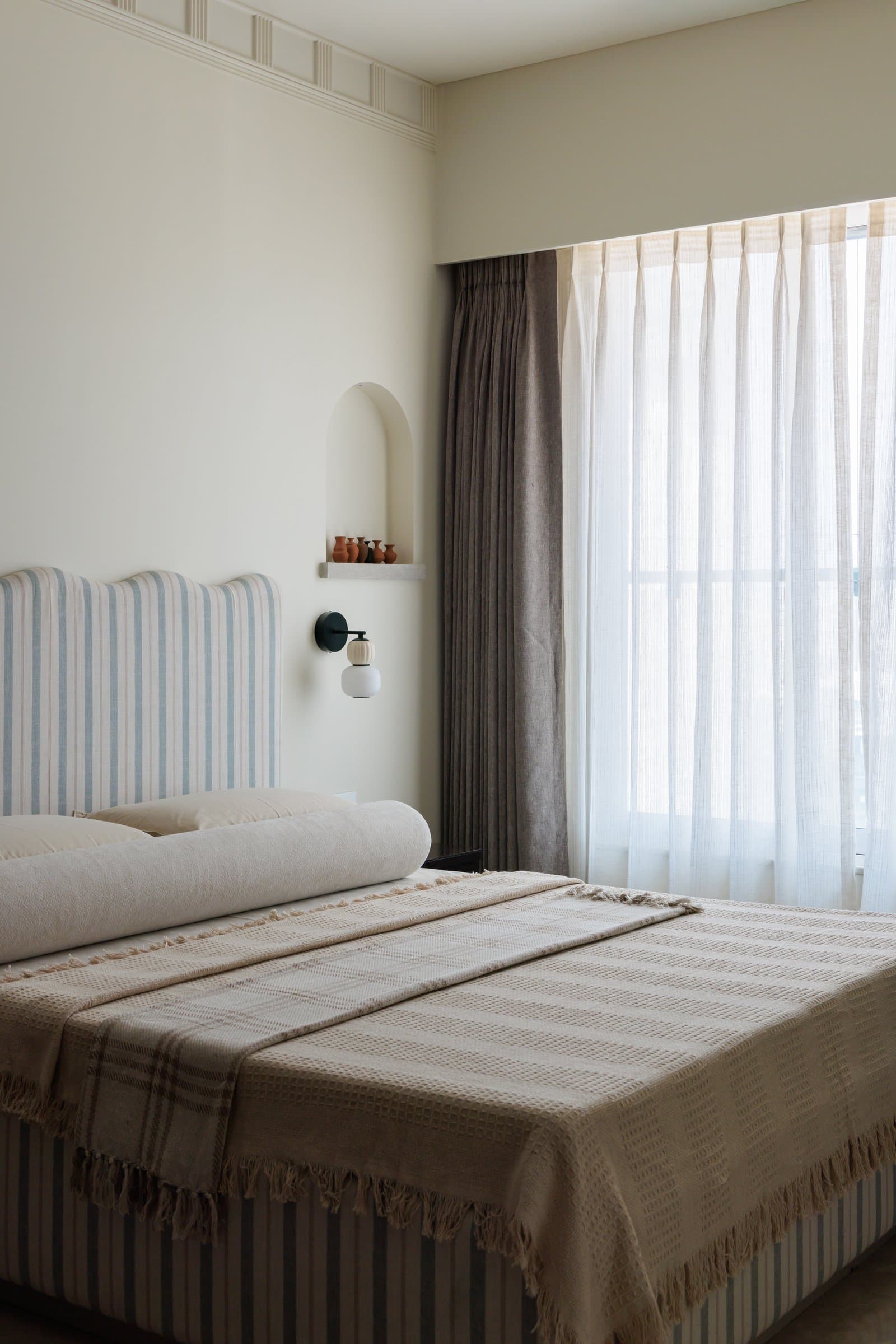 The second bedroom, where a striped upholstered headboard and a small arched wall niche set a lighter, more informal tone