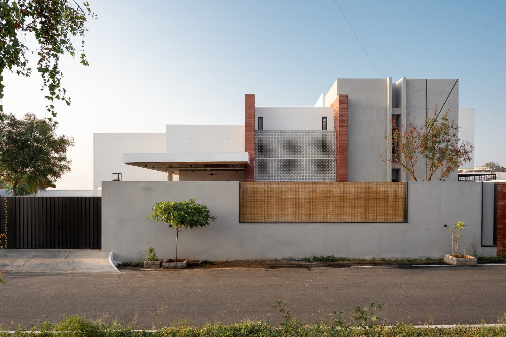 The street-facing elevation reads as grounded and regionally specific, grey concrete and patterned screen working at domestic scale