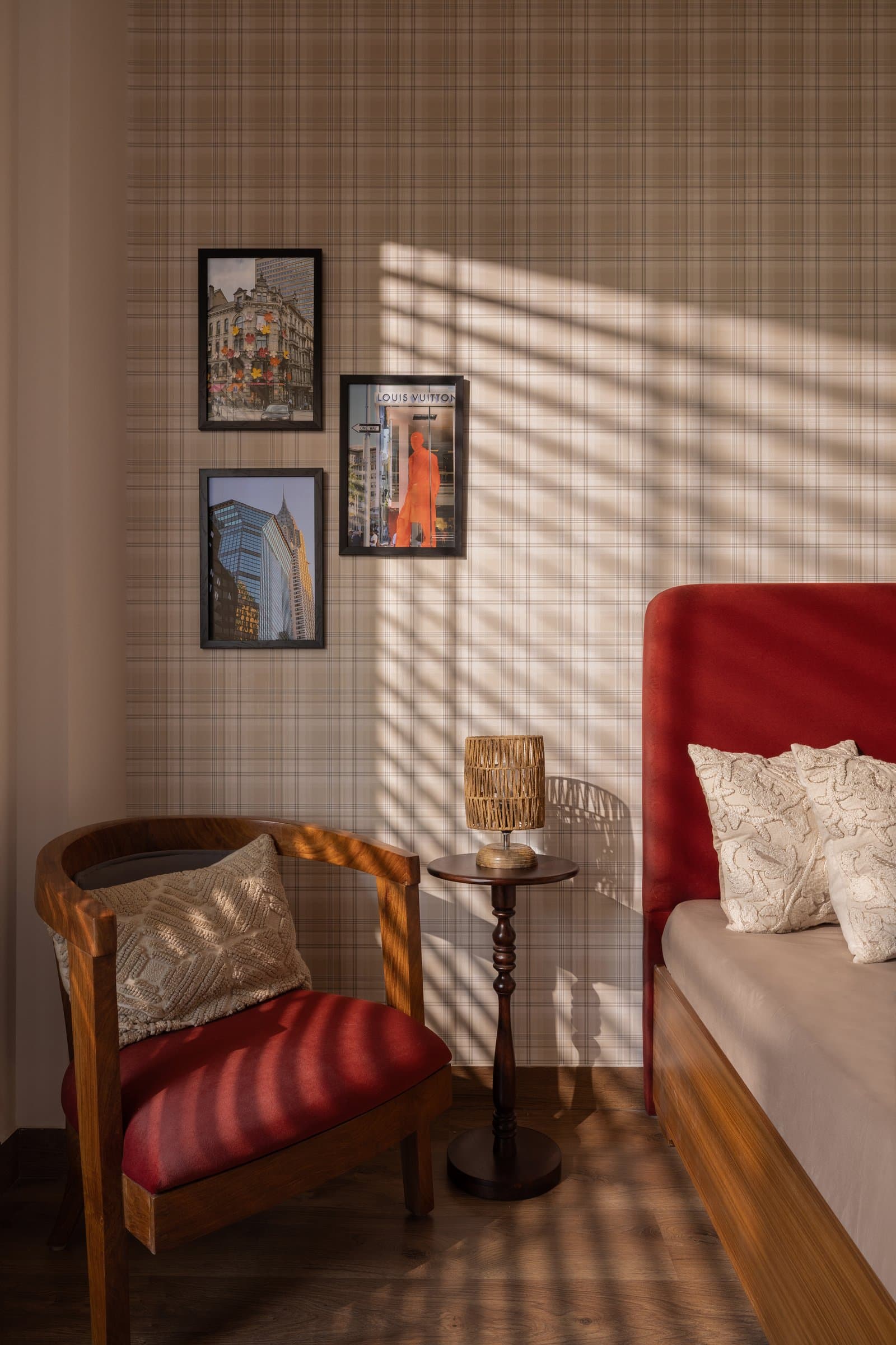The guest bedroom trades earth tones for plaid wallpaper and a red upholstered headboard, catching afternoon light