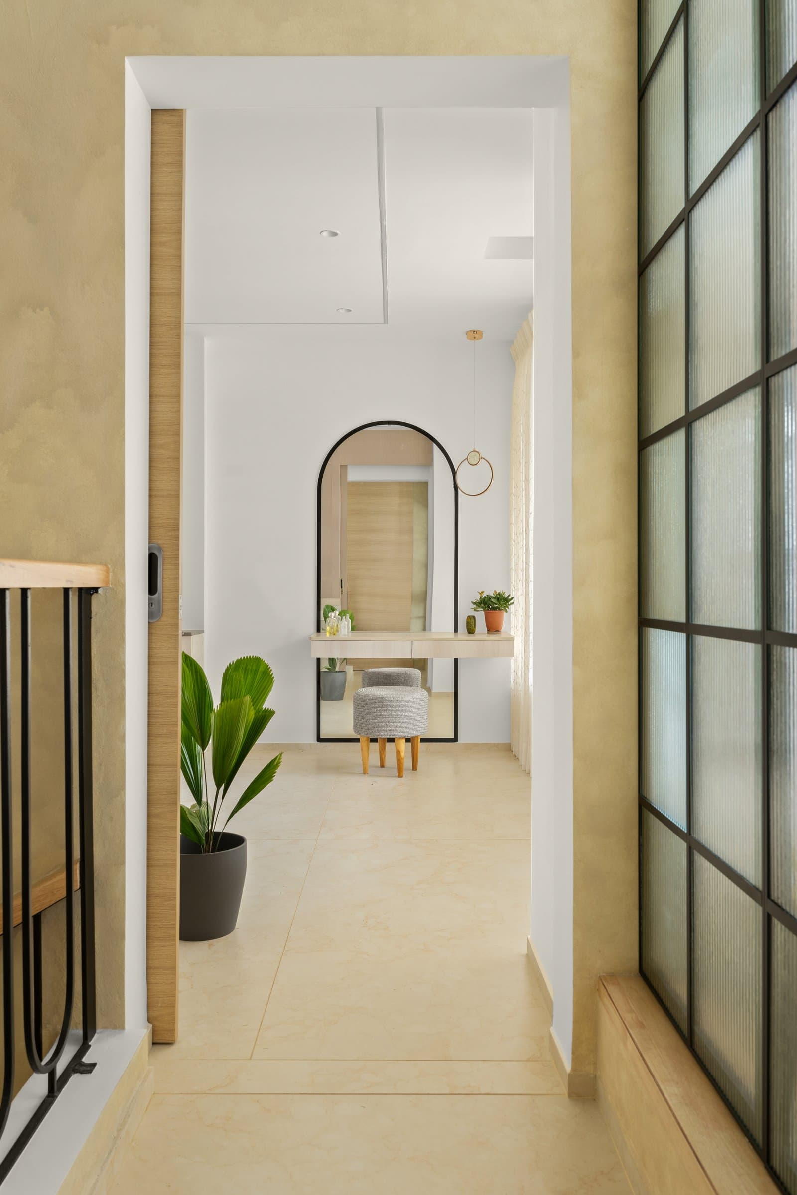 The upper passage: arched mirror, ringed pendant, and the same warm ochre plaster that threads the staircase below