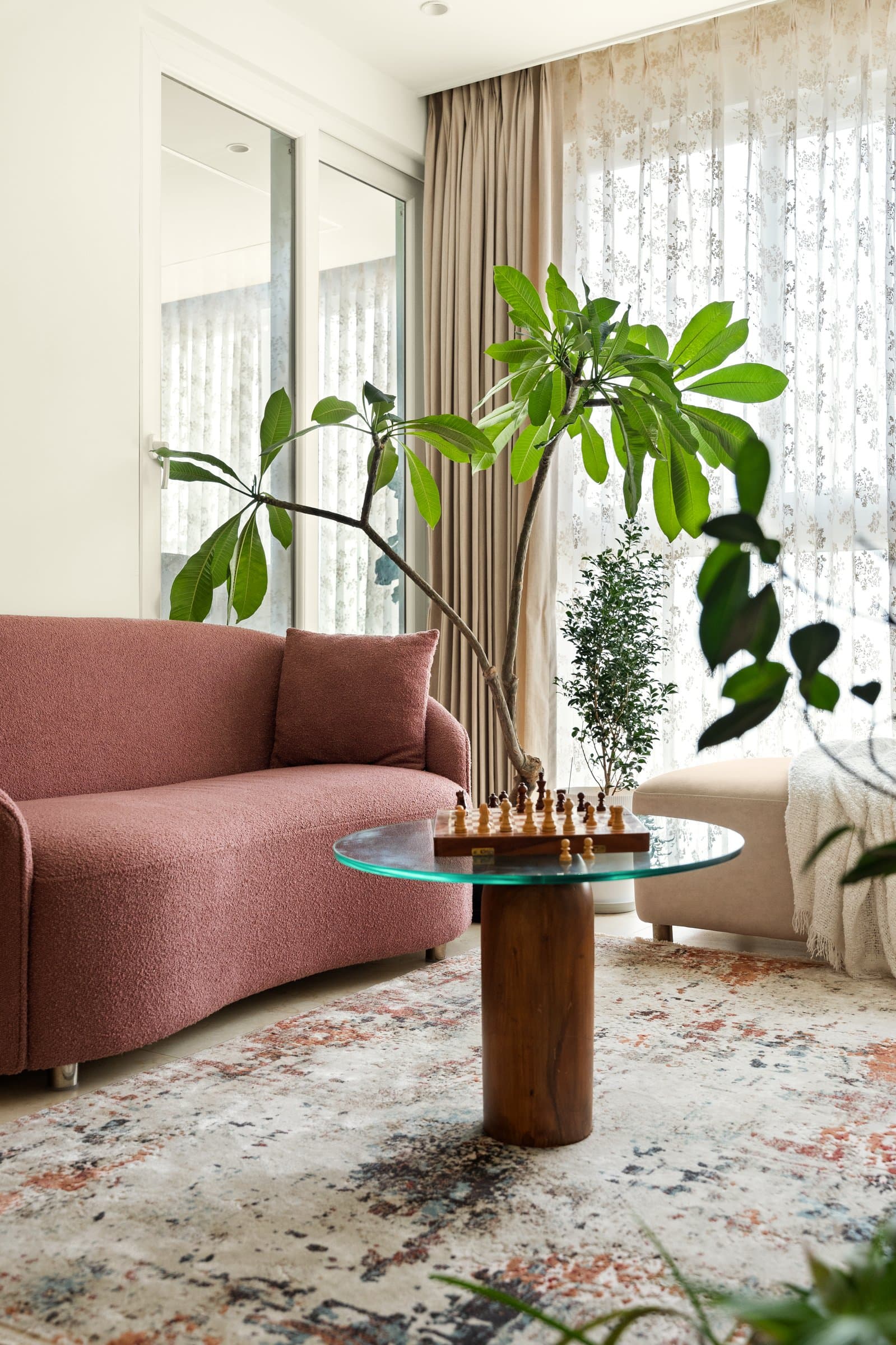 The dusty rose boucle sofa, the home's single chromatic assertion, held in check by glass, timber, and unhurried greenery