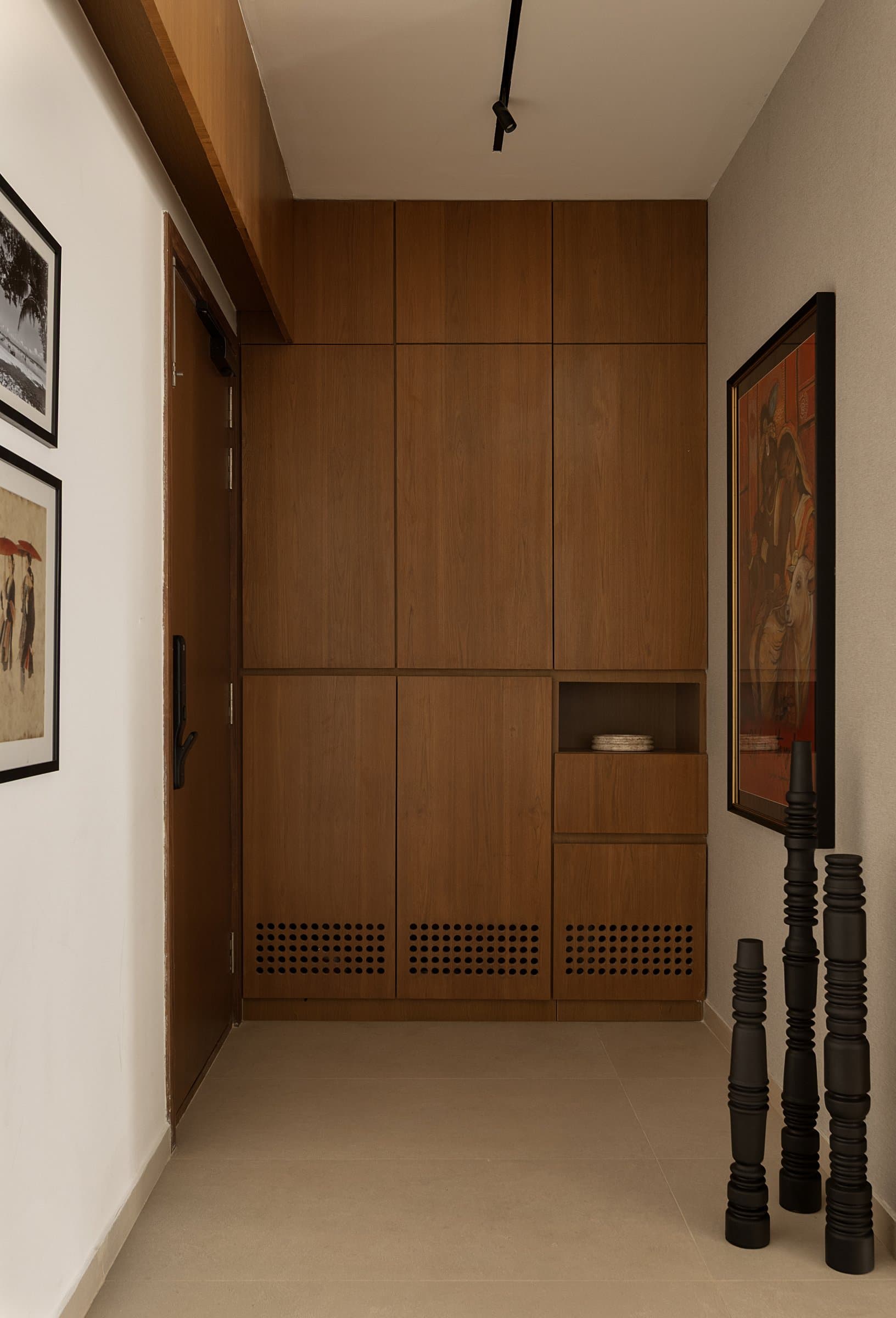 The foyer: a single composed plane in warm veneer absorbs shoe storage, ventilation, and display before the home properly begins