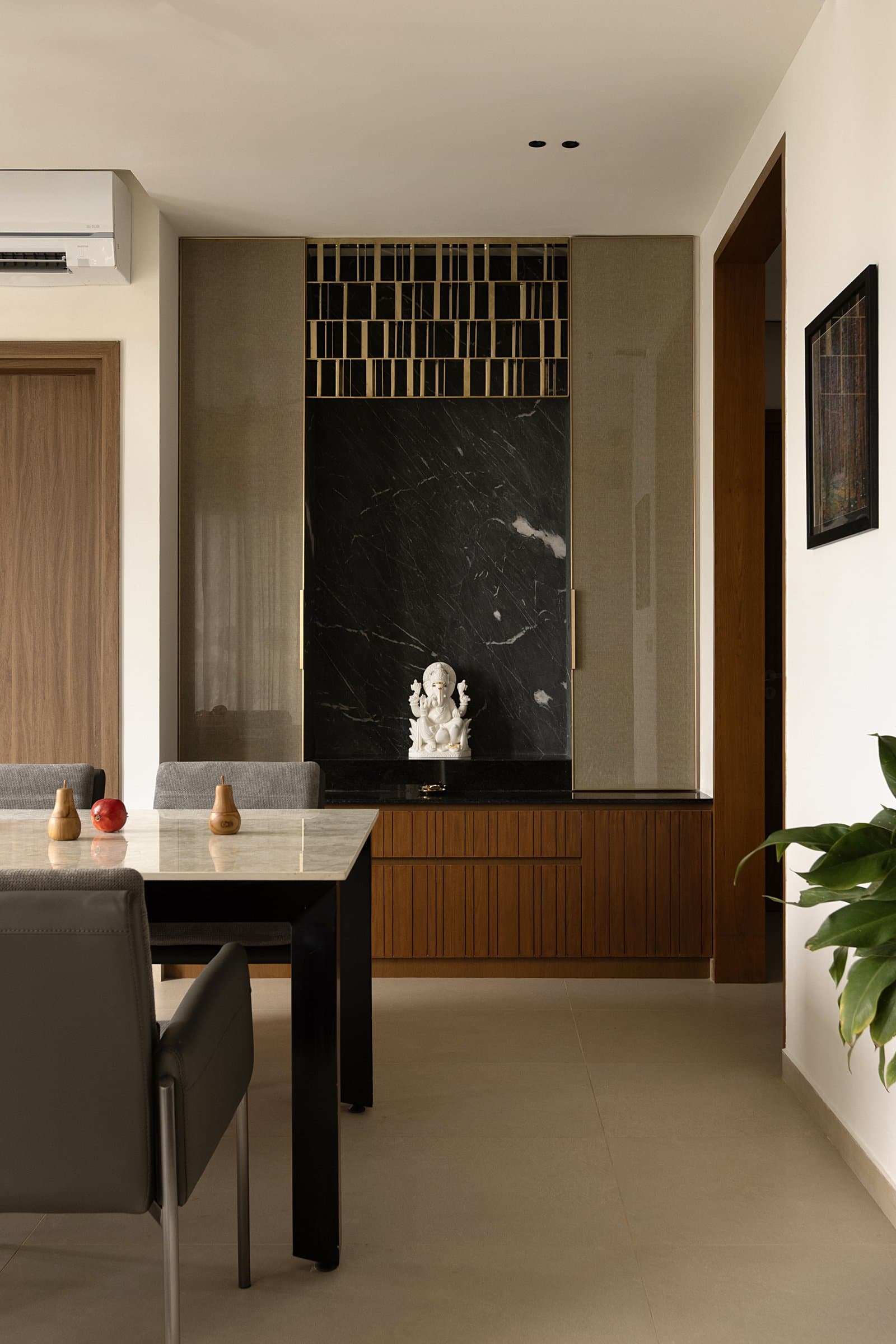 The puja room embedded in the dining wall: river-washed green-black marble framing the deity, brass jaali above