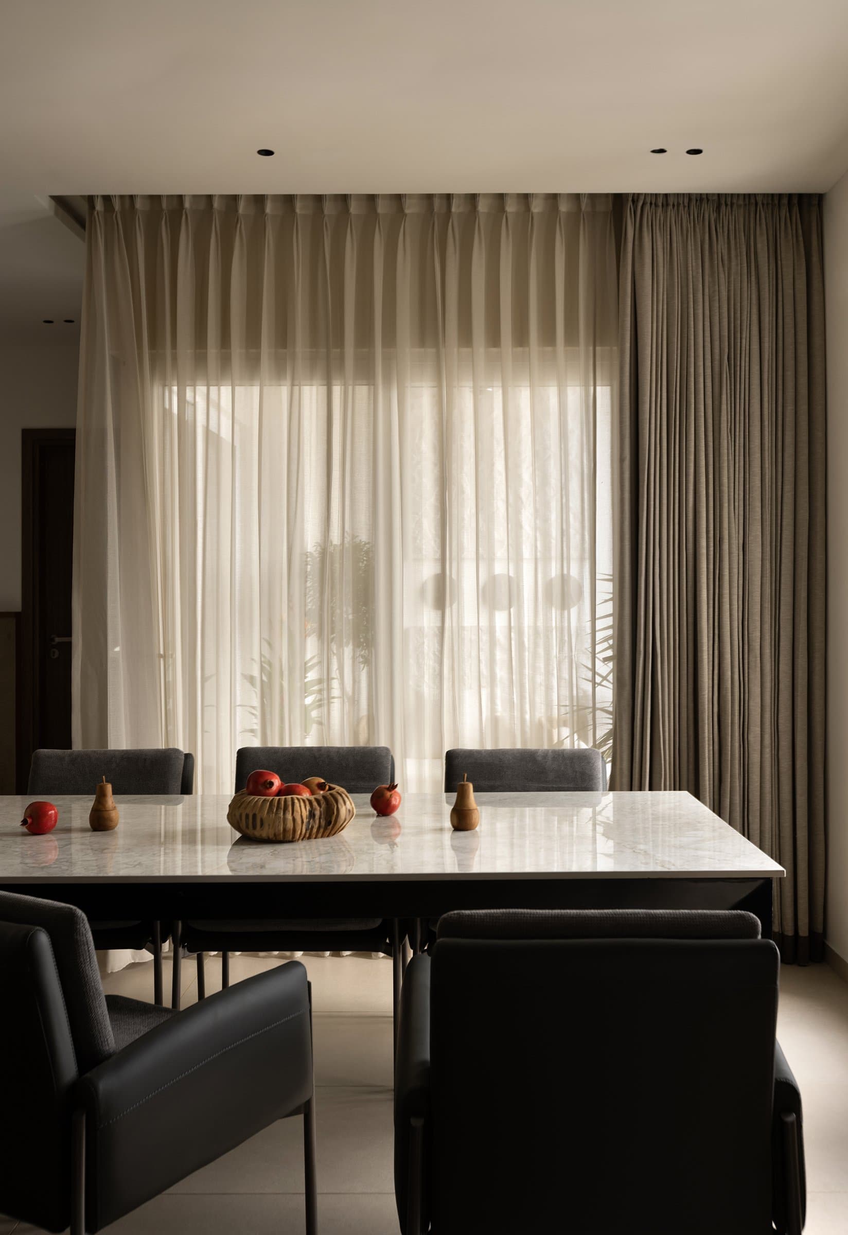 Layered sheer and taupe curtains filter Chennai's afternoon light onto a marble tabletop