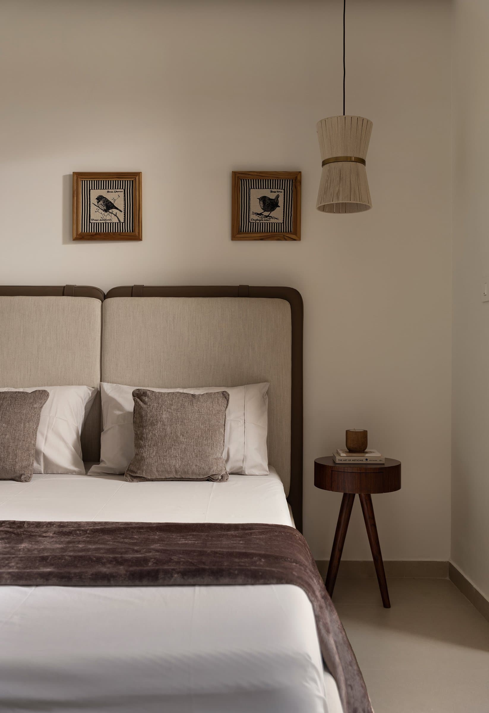 The guest bedroom keeps its gestures few: an upholstered linen headboard, two bird prints, a walnut side table