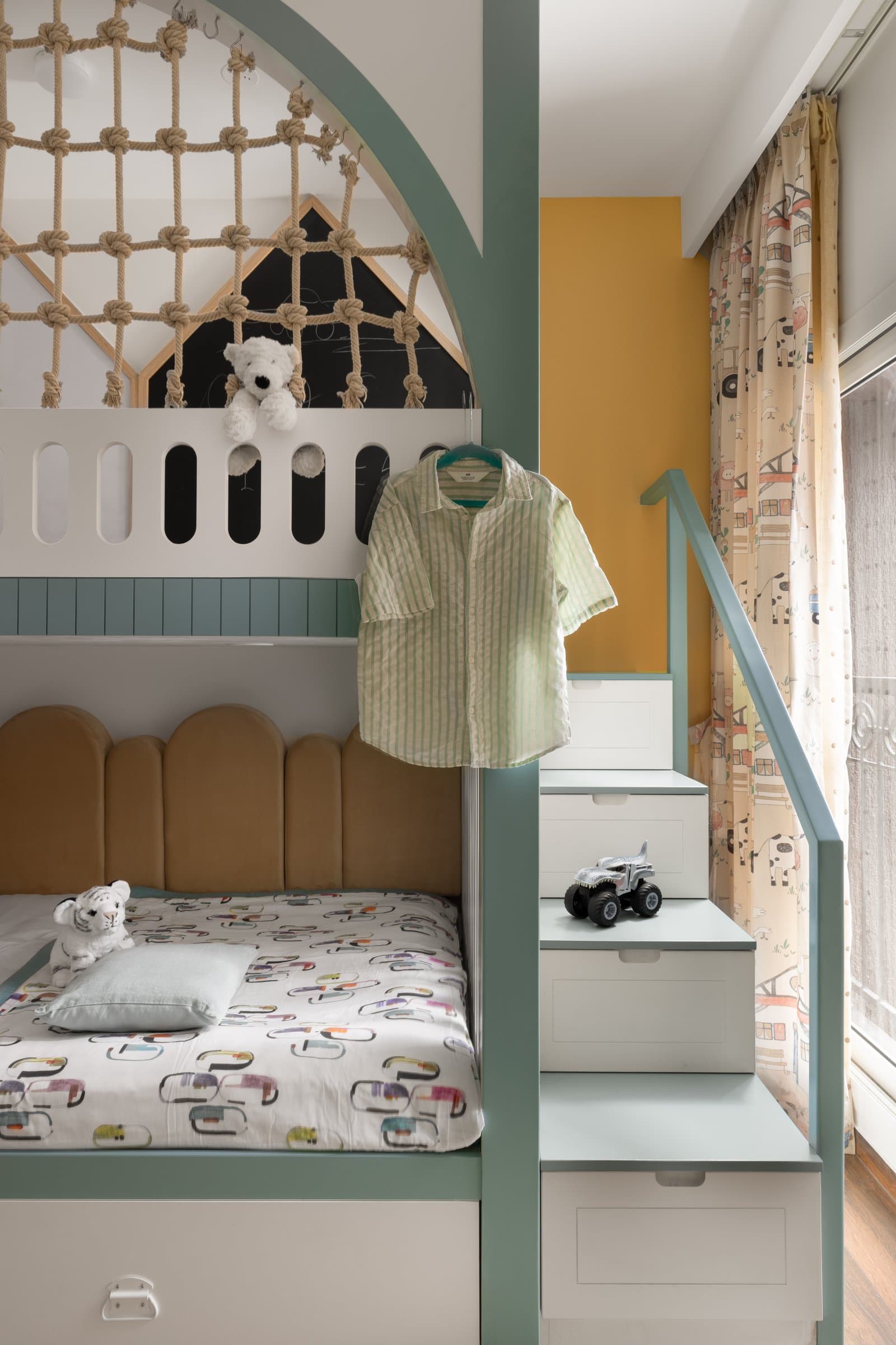 From the other side: a rope-net canopy, stepped storage drawers, and a scalloped velvet headboard make the bunk a piece of working play architecture