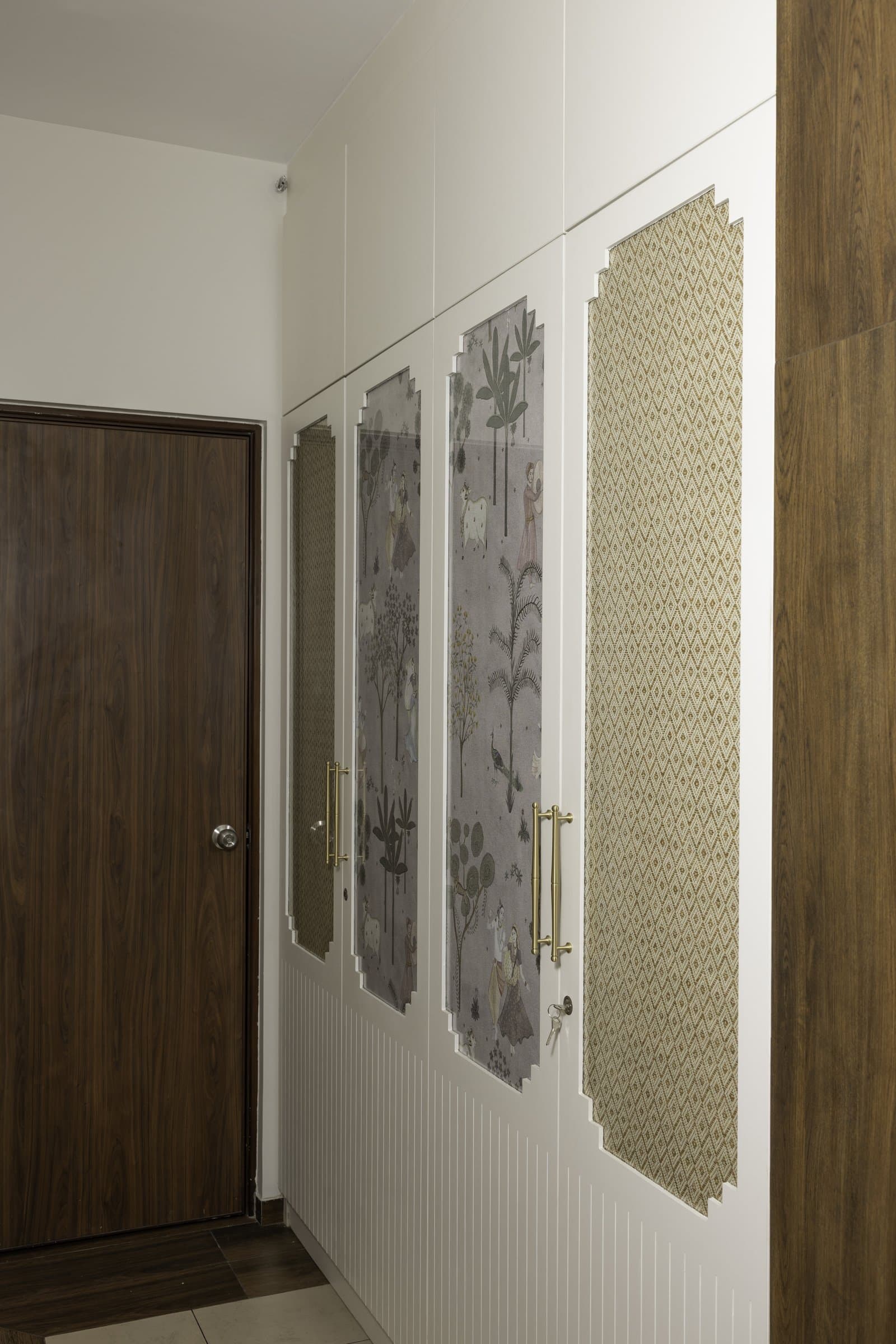 Pichwai-inspired panels framed by stepped white architraves turn entry storage into a quiet exhibition of heritage motifs