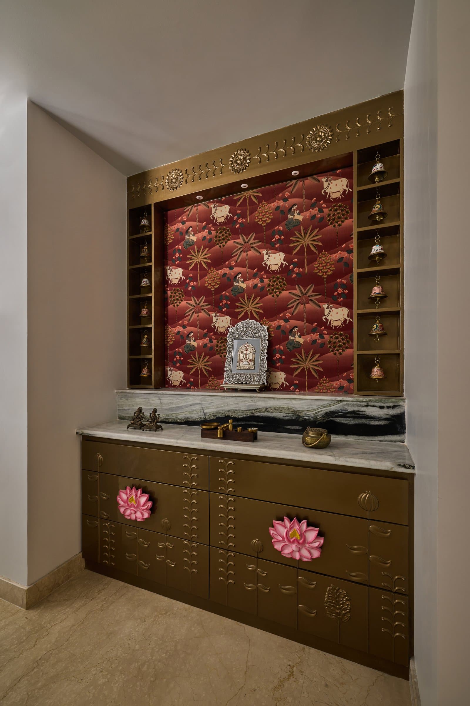The pooja niche: a printed Pichwai-style panel in deep red, framed by brass-clad shelving