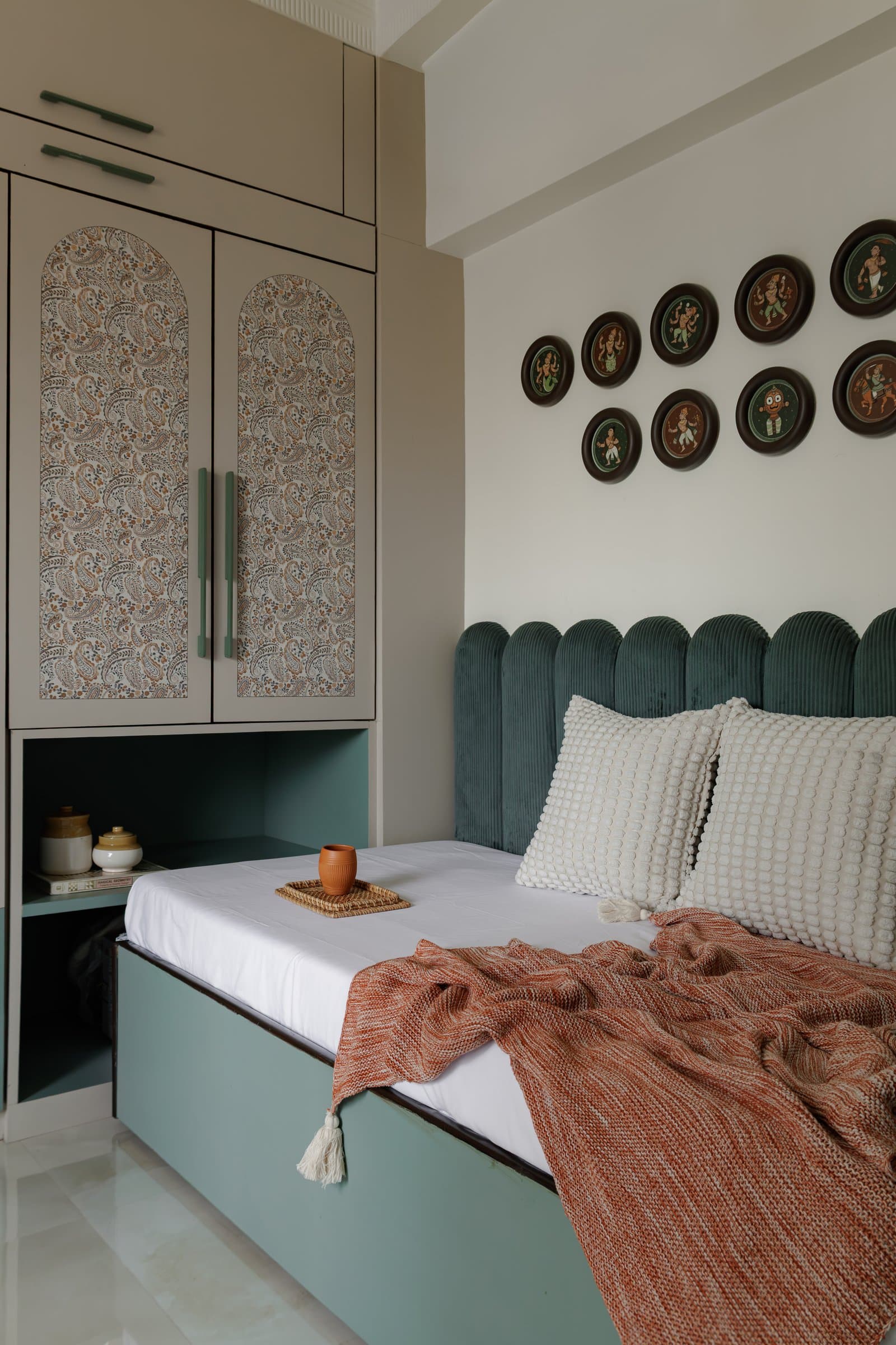 The guest bedroom, where a grid of Dashavatar paintings in the Konkan Ganjifa tradition presides over a sage and terracotta palette