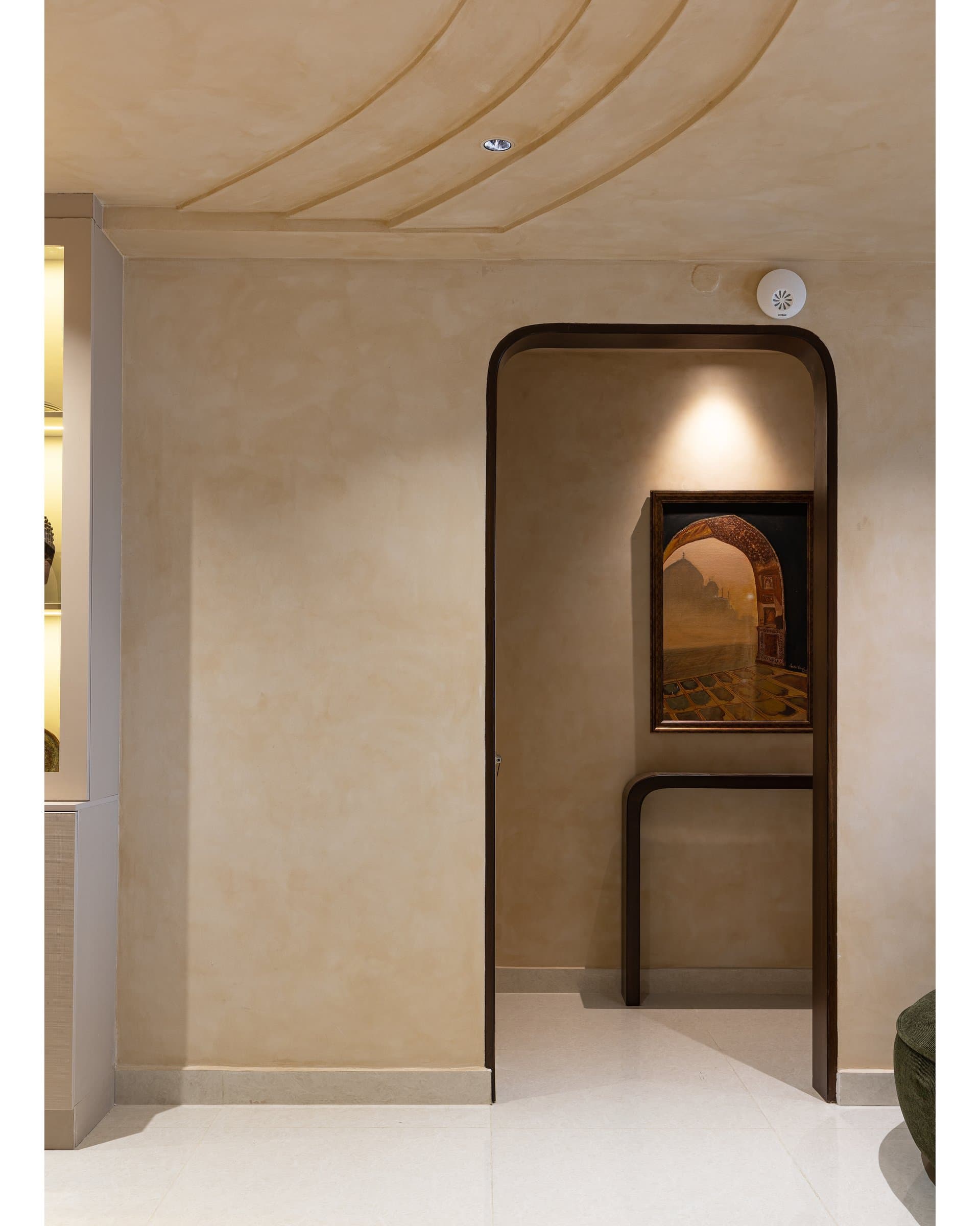 The arrival vestibule, where a rounded portal frames a small Mughal-arch painting and a curved console, introducing the home's limewash language