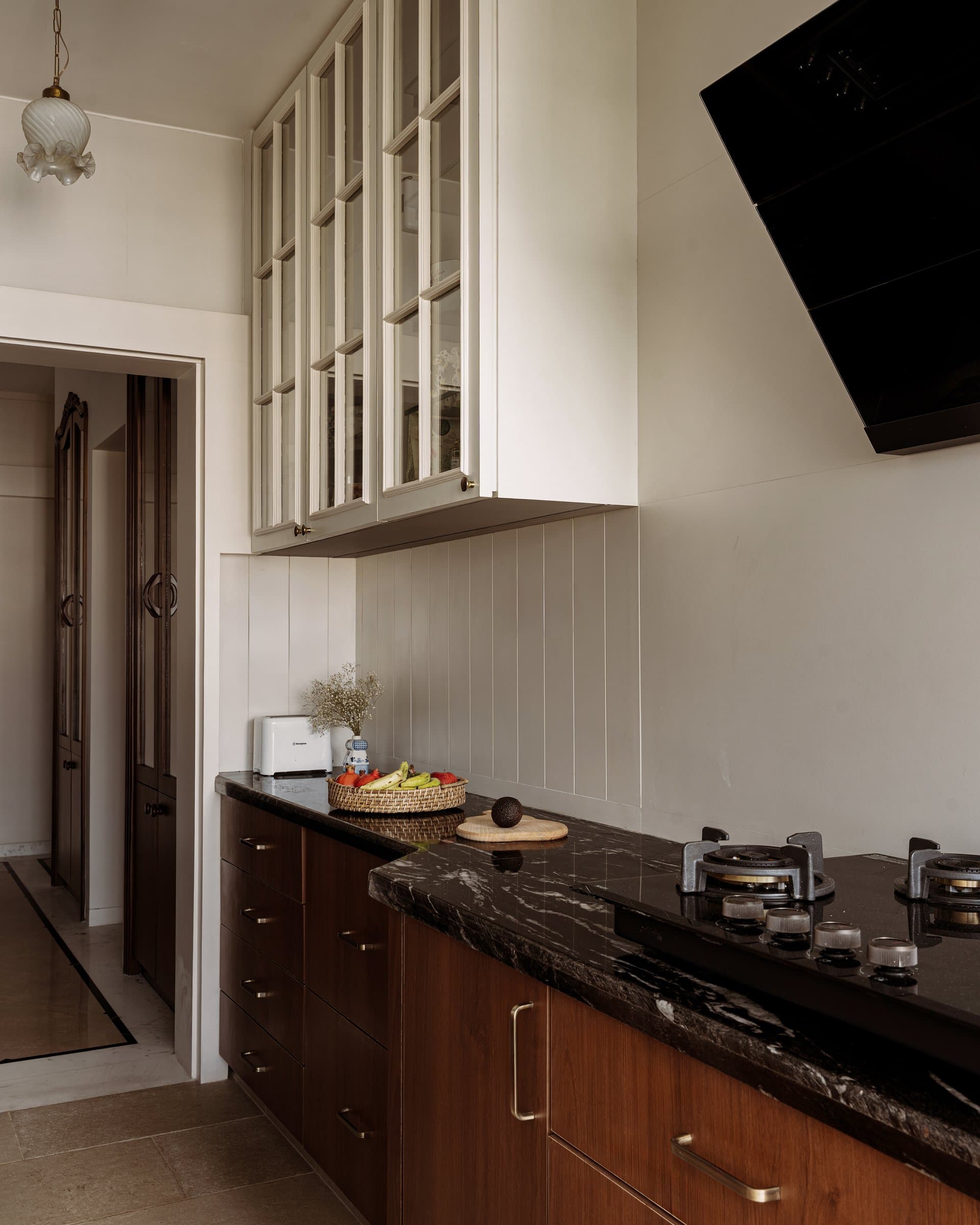The cooking run, where glass-fronted upper cabinets and a veined black stone counter carry the home's discipline into its most utilitarian room