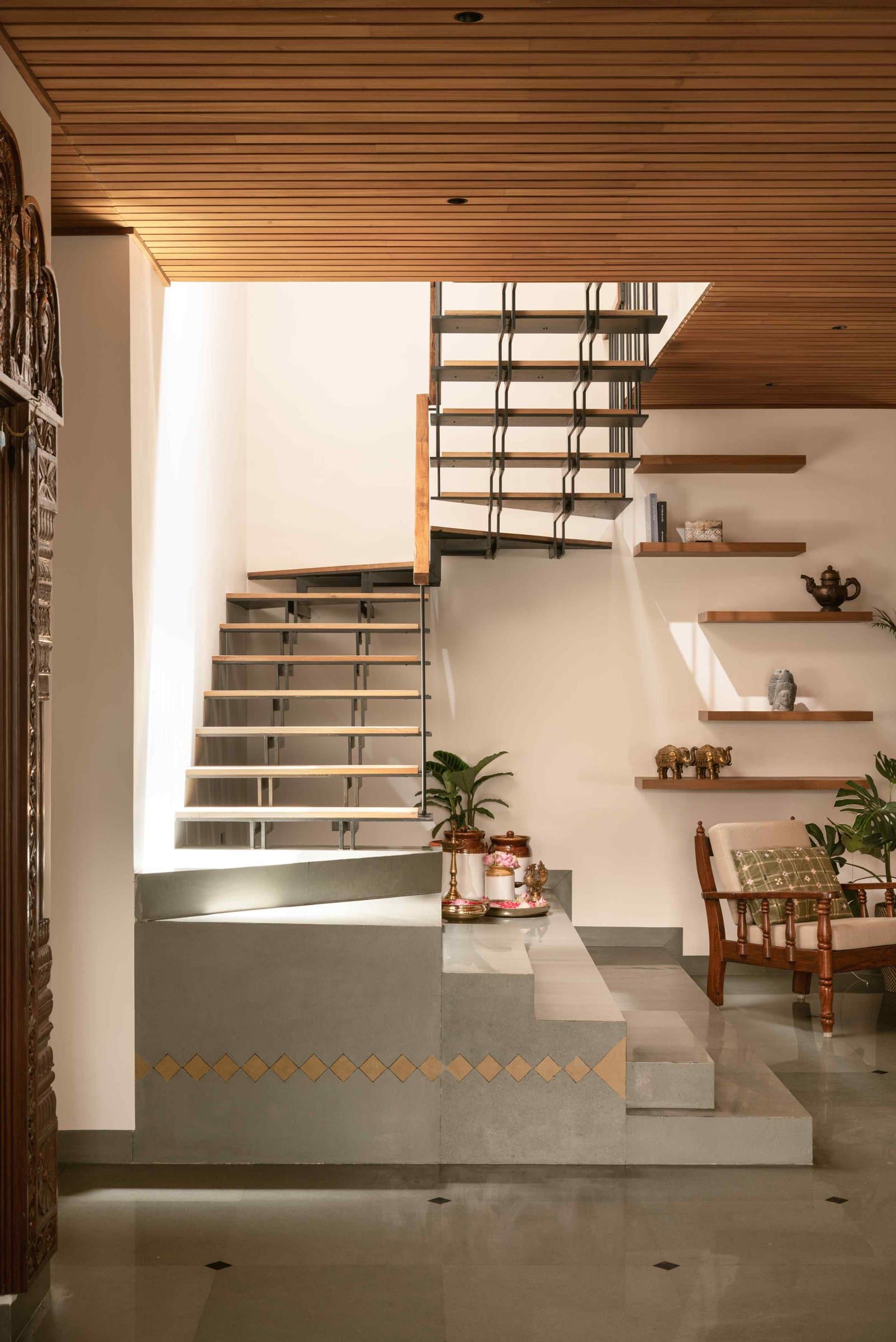 The reorganised staircase: folded metal stringers, a pigmented concrete plinth, and a wall of cantilevered display shelves